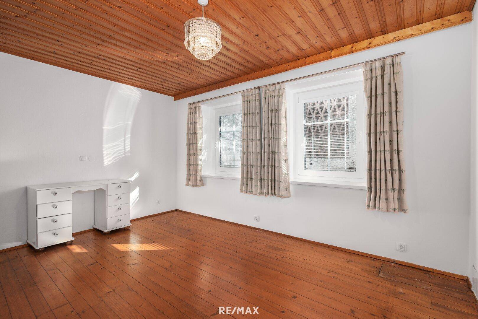 Geräumiges Schlafzimmer mit Holzdecke, Parkettboden und zwei Fenstern.
