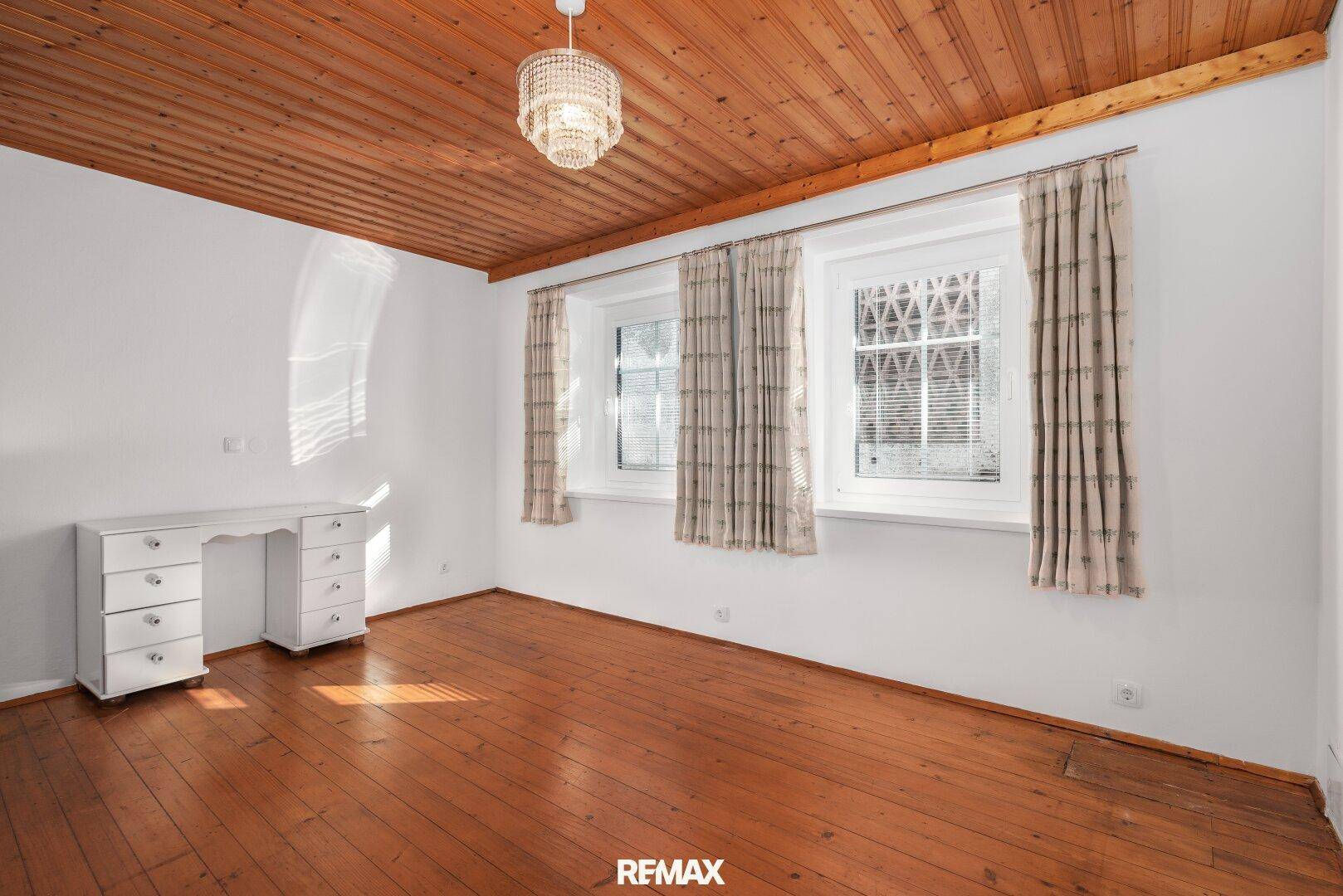 Geräumiger Raum mit Holzdielenboden, Holzdecke und Fenstern, ideal als Schlafzimmer.