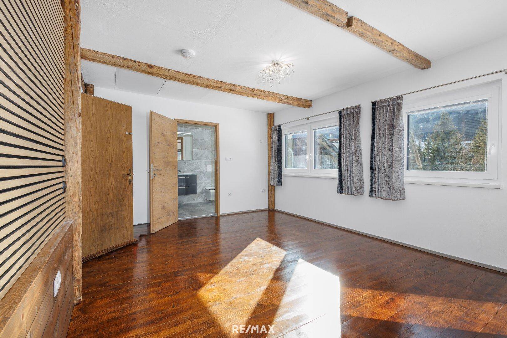 Geräumiges Schlafzimmer mit Holzbalken, Parkettboden und Zugang zu einem modernen Badezimmer.