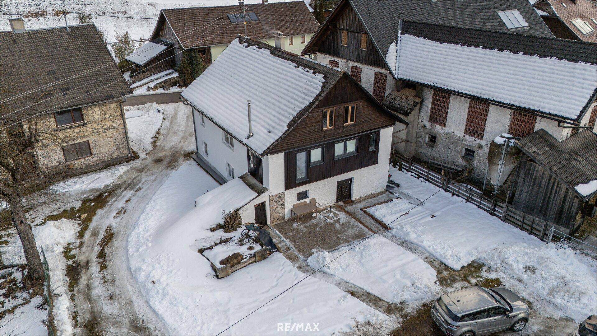 Vogelperspektive des Hauses mit dunklem Holzgiebel und verschneitem Grundstück.