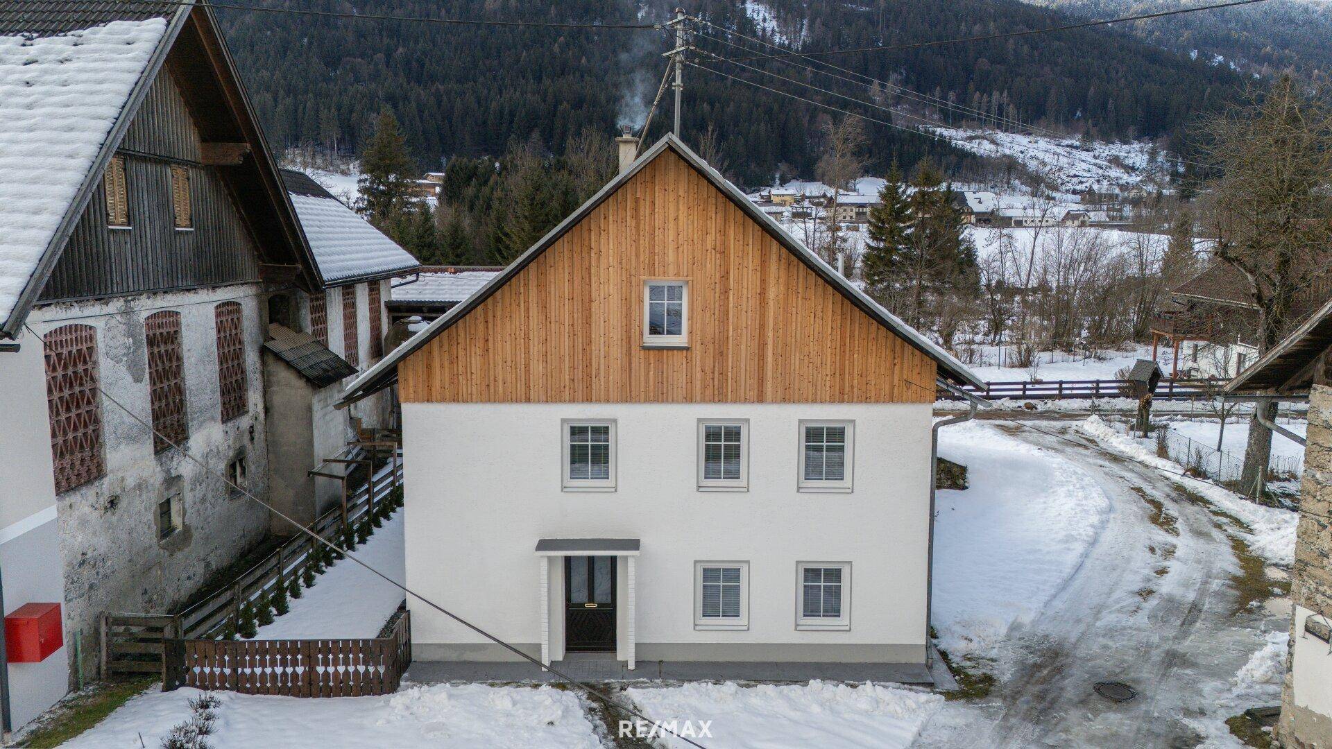 Vorderansicht des Hauses mit weißer Fassade, Holzgiebel und verschneiter Umgebung.
