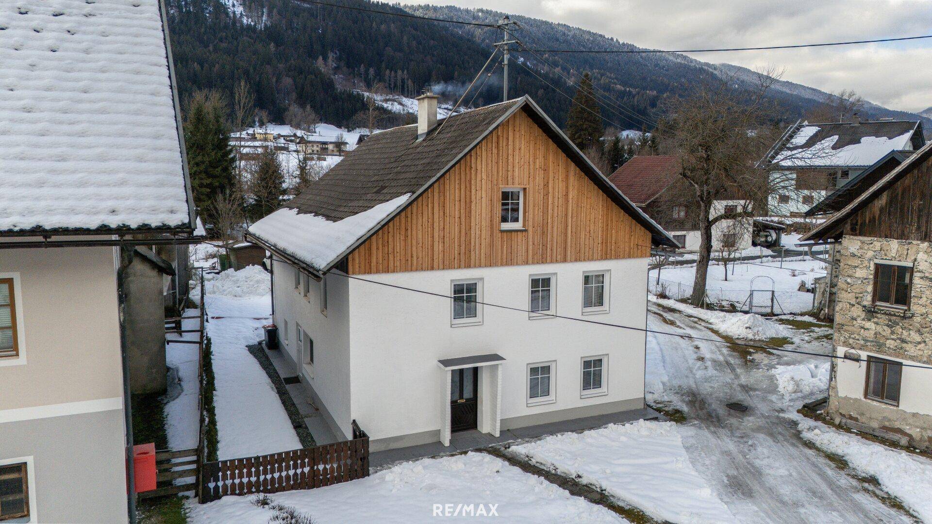 Seitenansicht des Hauses mit weißer Fassade, Holzgiebel und verschneiter Umgebung.