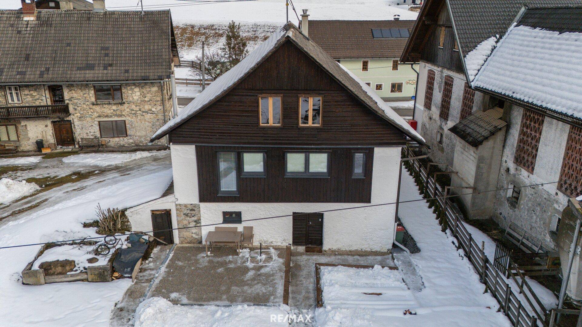 Rückansicht des Hauses mit dunklem Holzgiebel und kleiner Terrasse im Schnee.