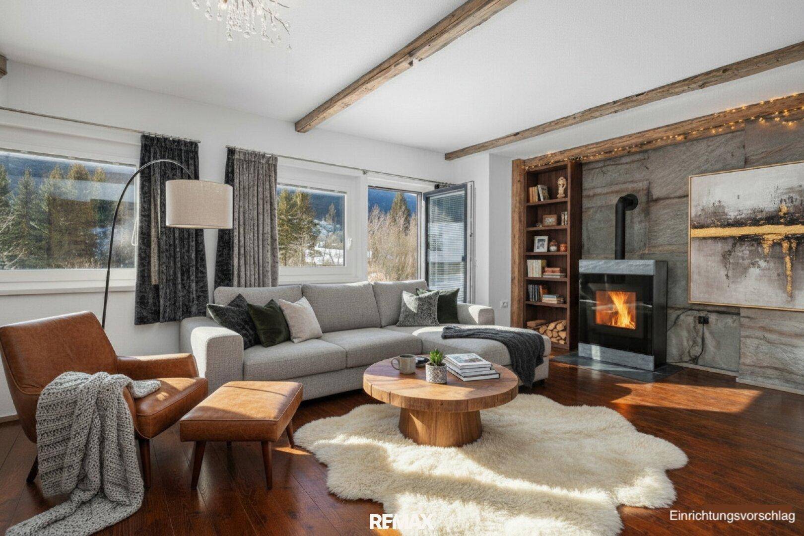 Gemütliches Wohnzimmer mit Kamin, Holzbalken und Blick auf die verschneite Landschaft.