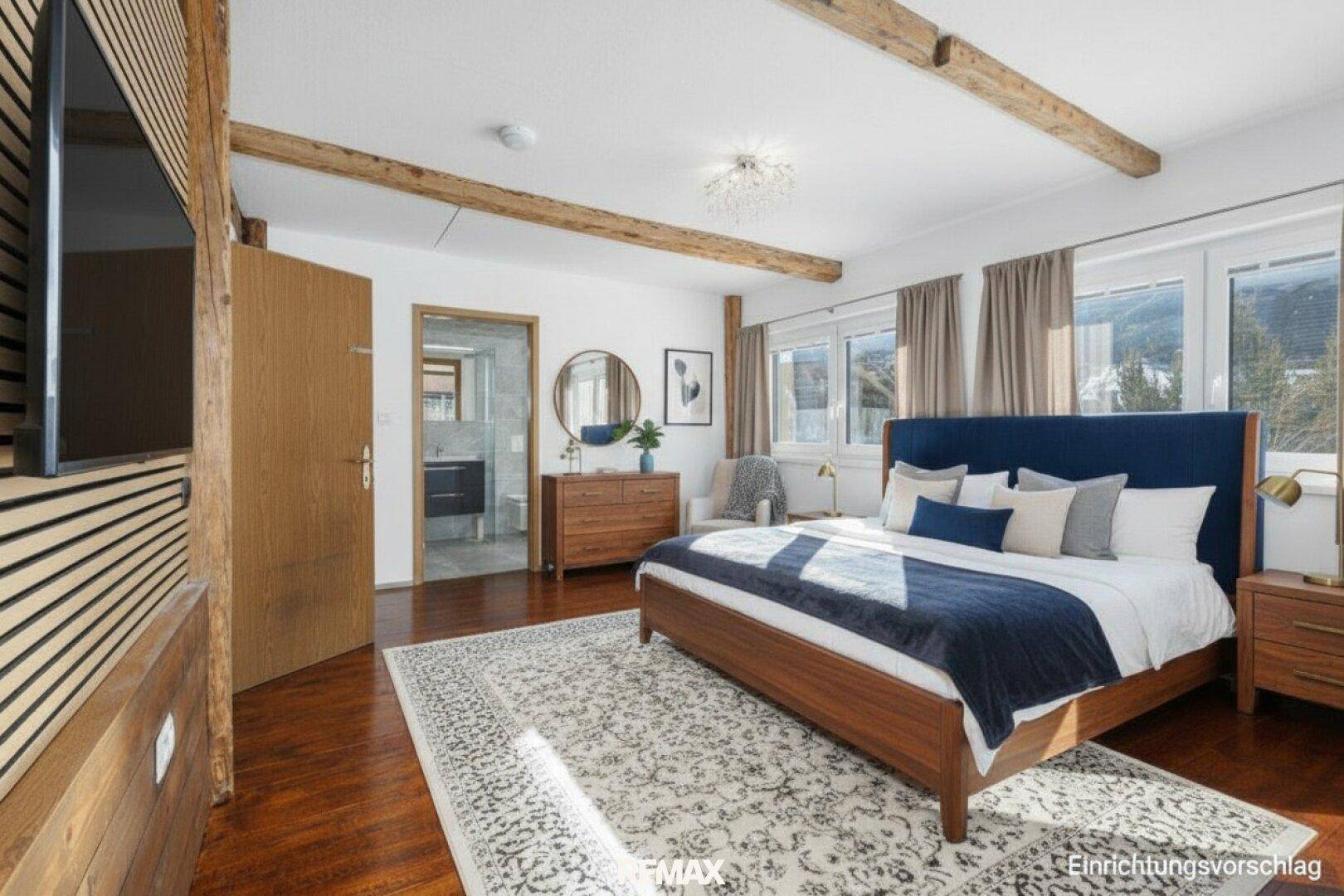 Helles Schlafzimmer mit Holzboden, sichtbaren Balken und direktem Zugang zum Badezimmer.