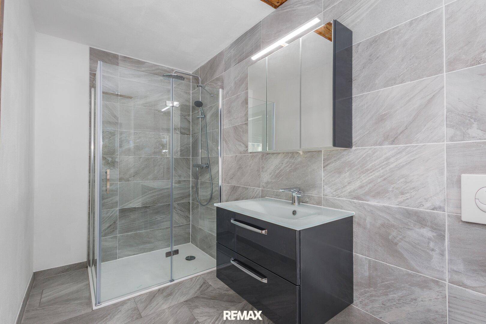 Modernes Badezimmer mit grauen Fliesen, begehbarer Dusche und stilvollem Waschtisch.
