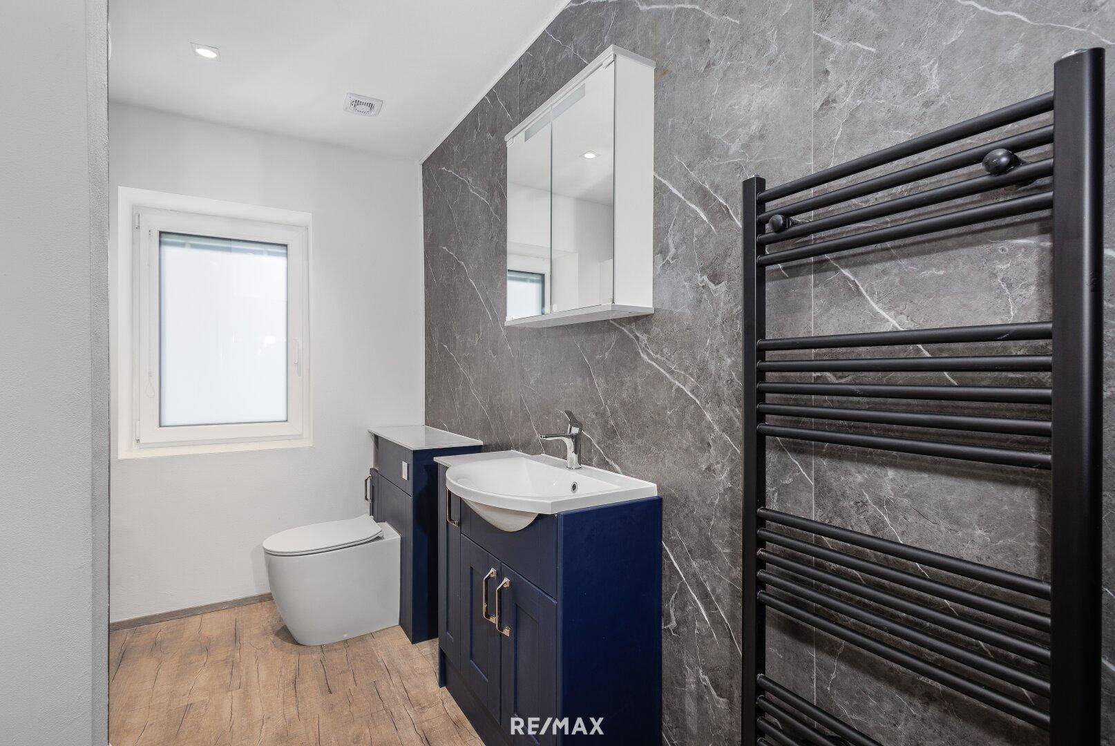 Modernes Badezimmer mit dunklen Marmorfliesen, Waschtisch, WC und beheiztem Handtuchhalter.