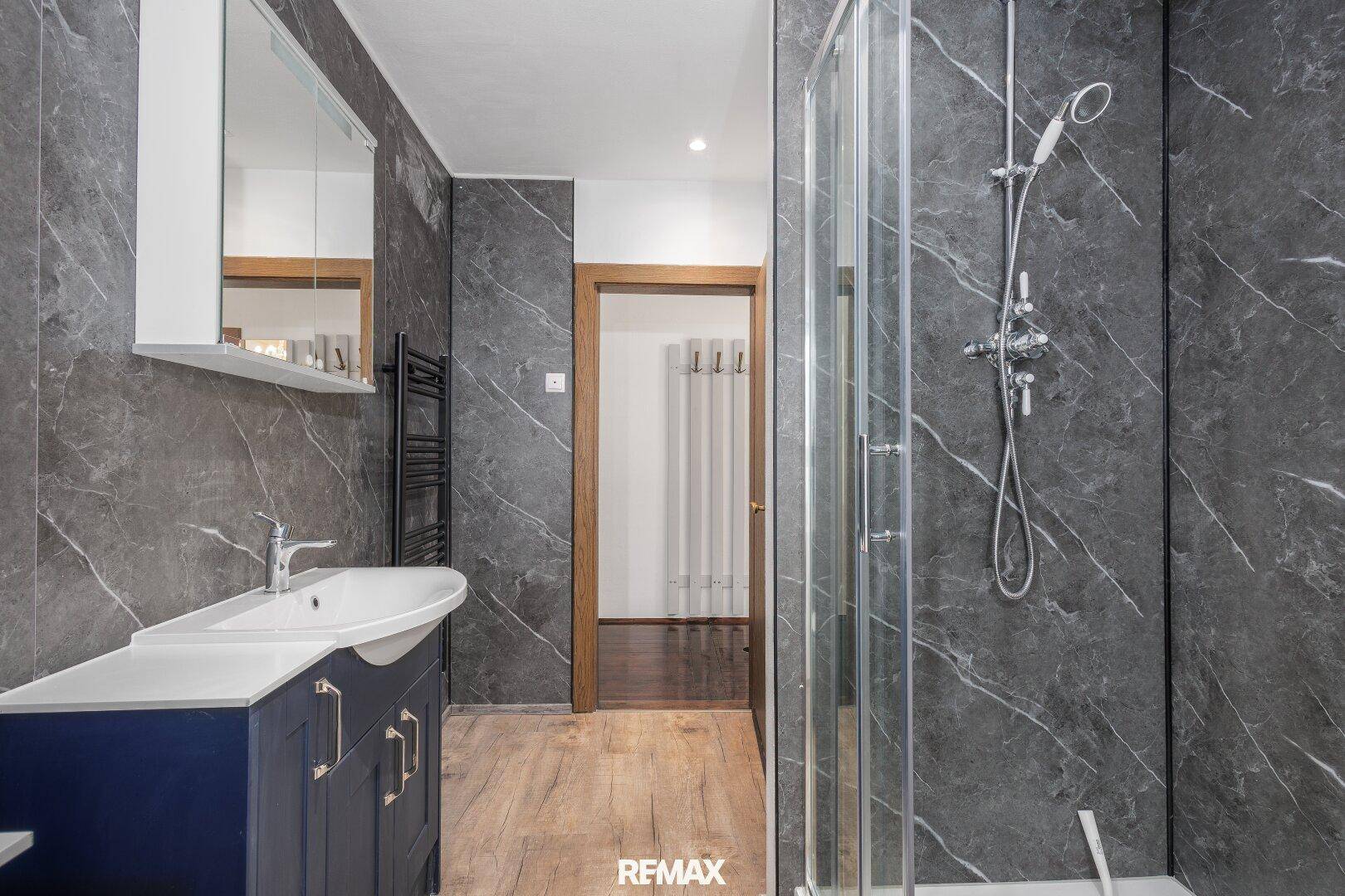 Modernes Badezimmer mit begehbarer Dusche, dunkelblauem Waschtisch und Marmor-Effekt-Fliesen.
