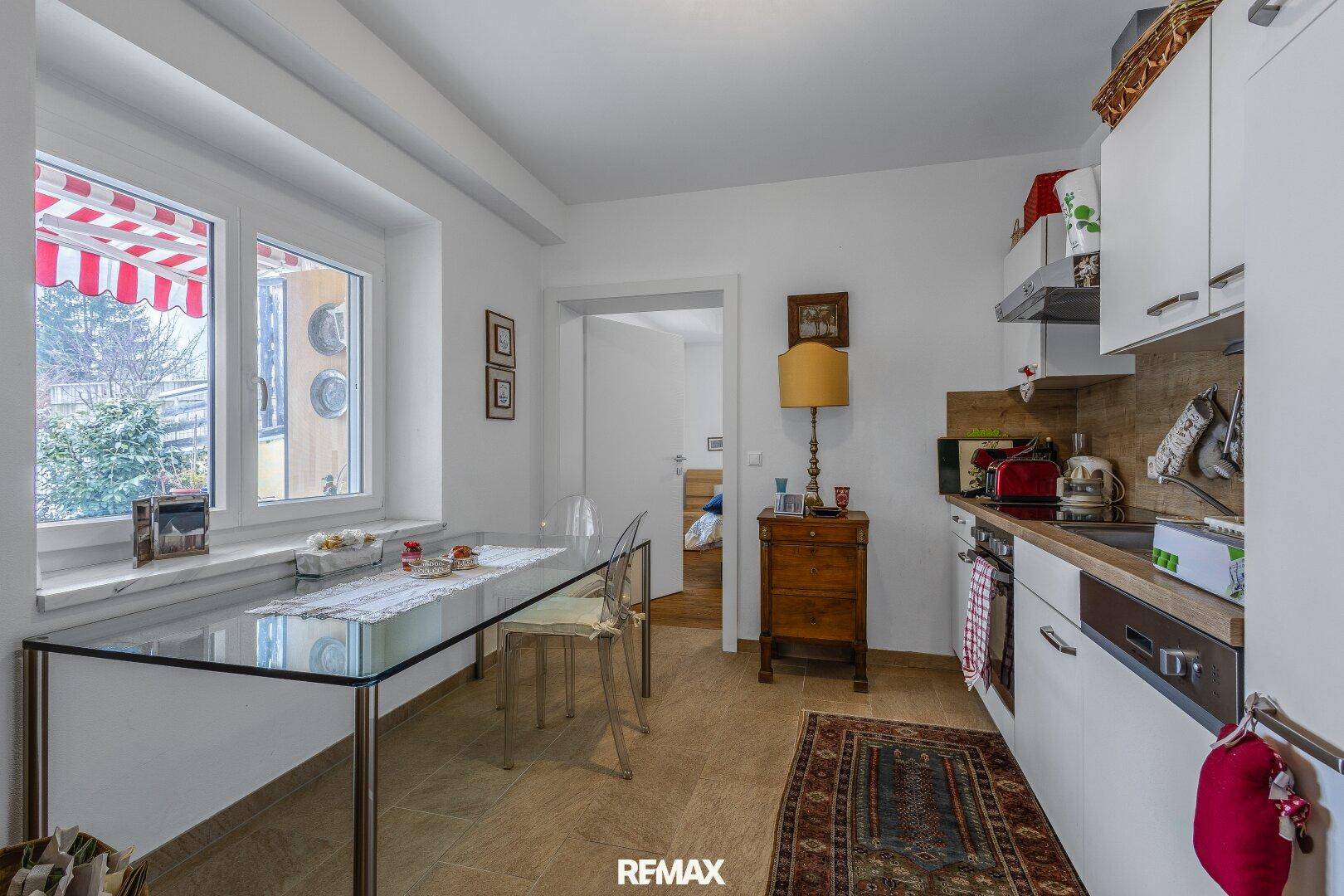 Funktionale Küche mit weißer Einrichtung, Essbereich und Fenster mit Blick nach draußen.
