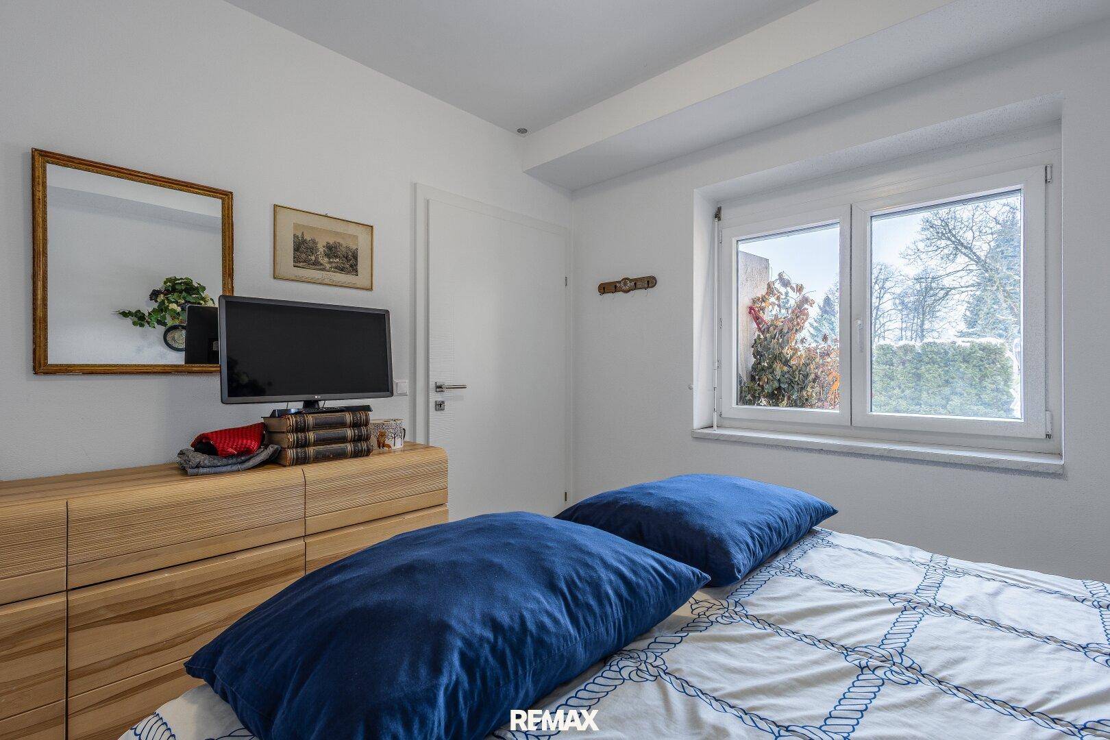 Helles Schlafzimmer mit Holzkleiderschrank, Doppelbett und Fensterblick ins Grüne.