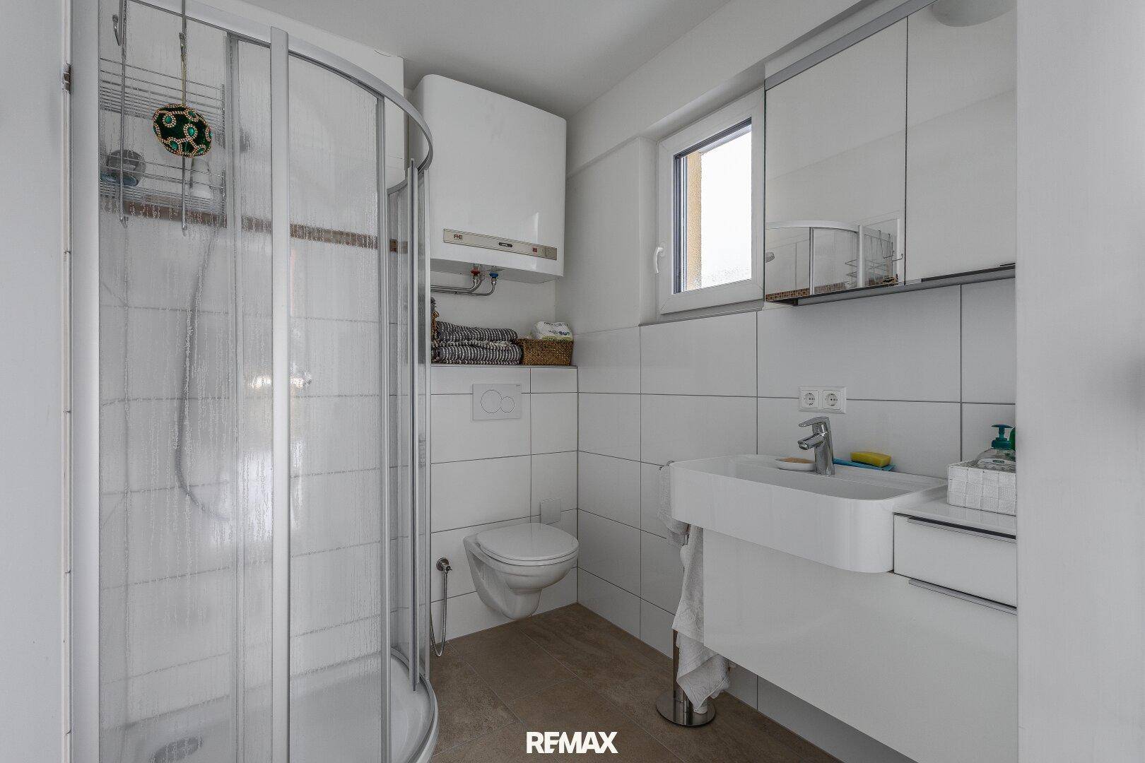 Helles Badezimmer mit Duschkabine, WC, Waschbecken und Fenster.