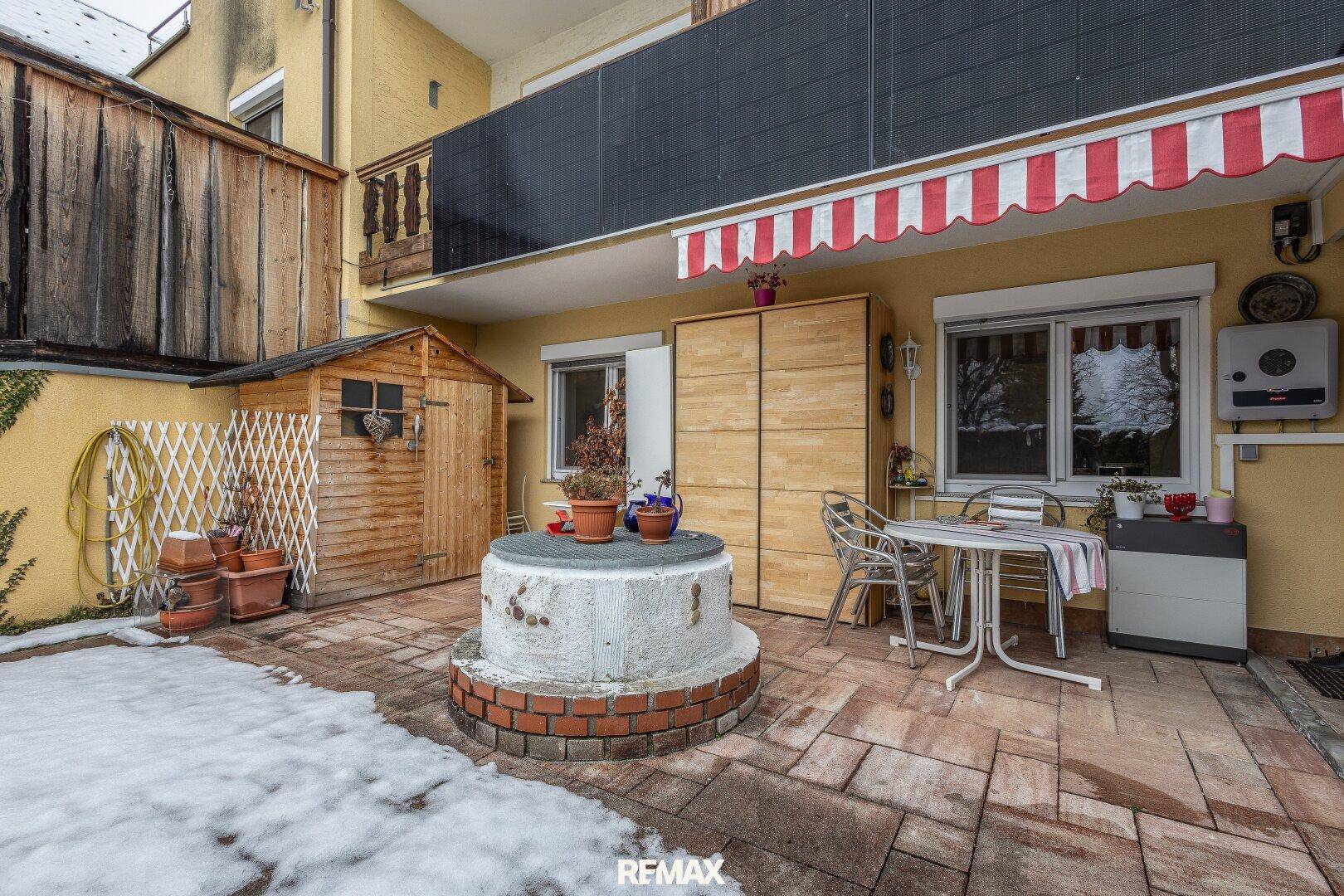 Außenbereich mit gepflasterter Terrasse, Gartenhaus und Sitzgelegenheiten im Schnee.