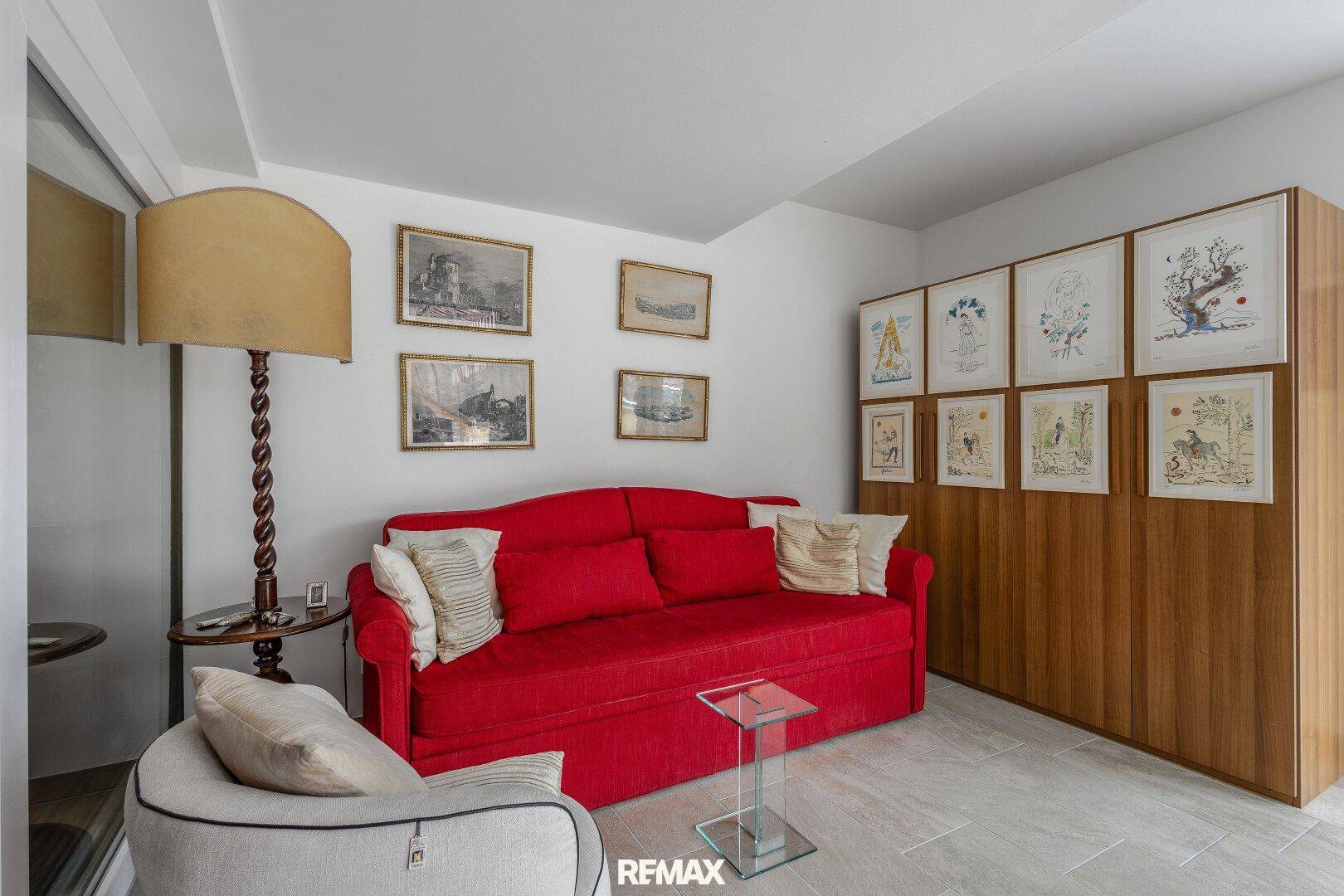 Gemütliches Wohnzimmer mit rotem Sofa, Stehlampe und einer Bilderwand.