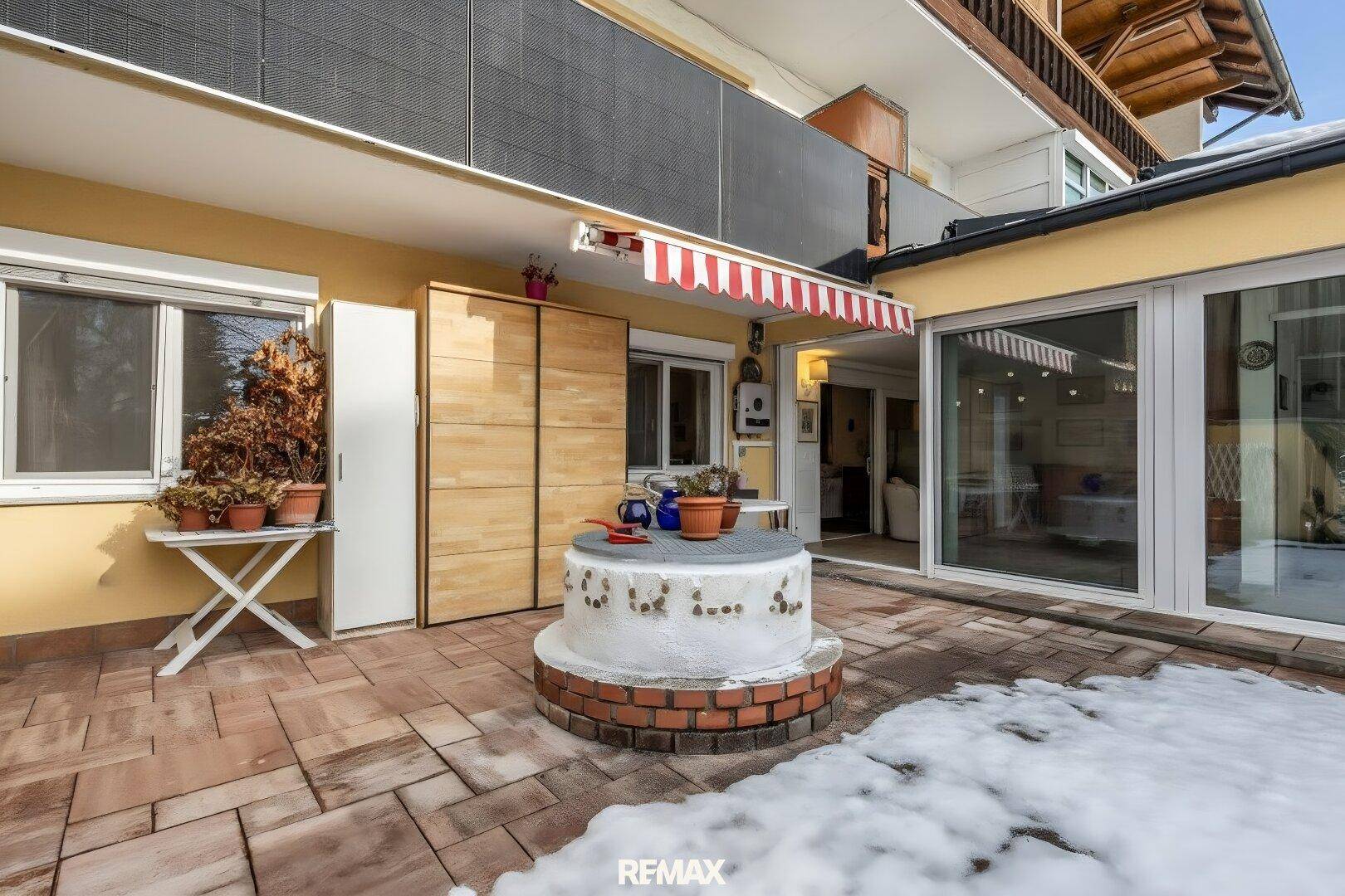 Geräumige Terrasse mit gepflastertem Boden, dekorativem Brunnen und Zugang zum Haus.