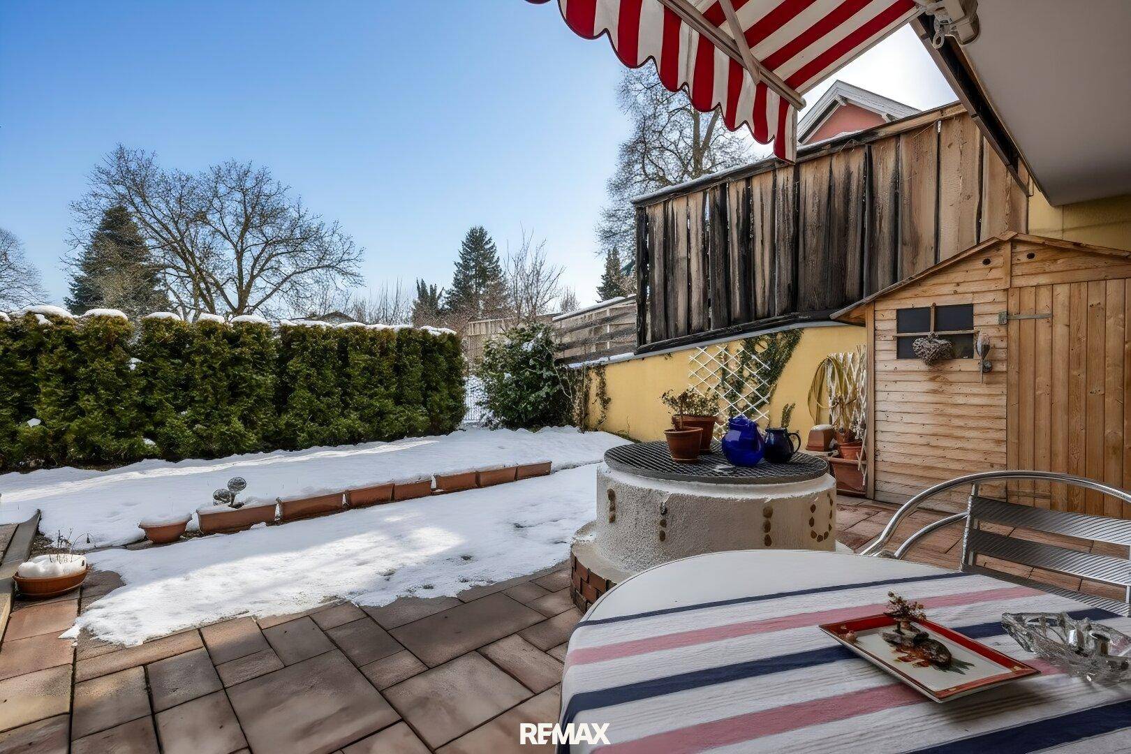 Terrasse mit Gartenmöbeln, Markise und Blick auf den verschneiten Garten mit Hecke.