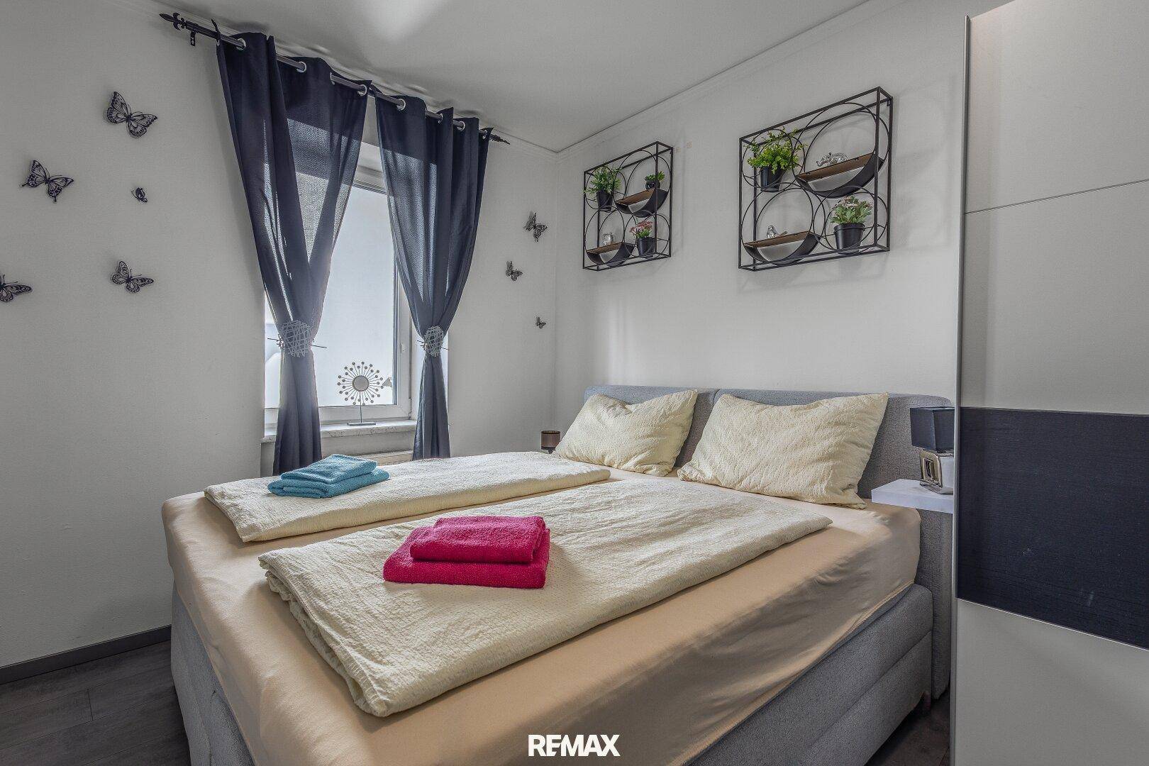 Gemütliches Schlafzimmer mit Doppelbett, dunklen Vorhängen und dekorativen Wandregalen.