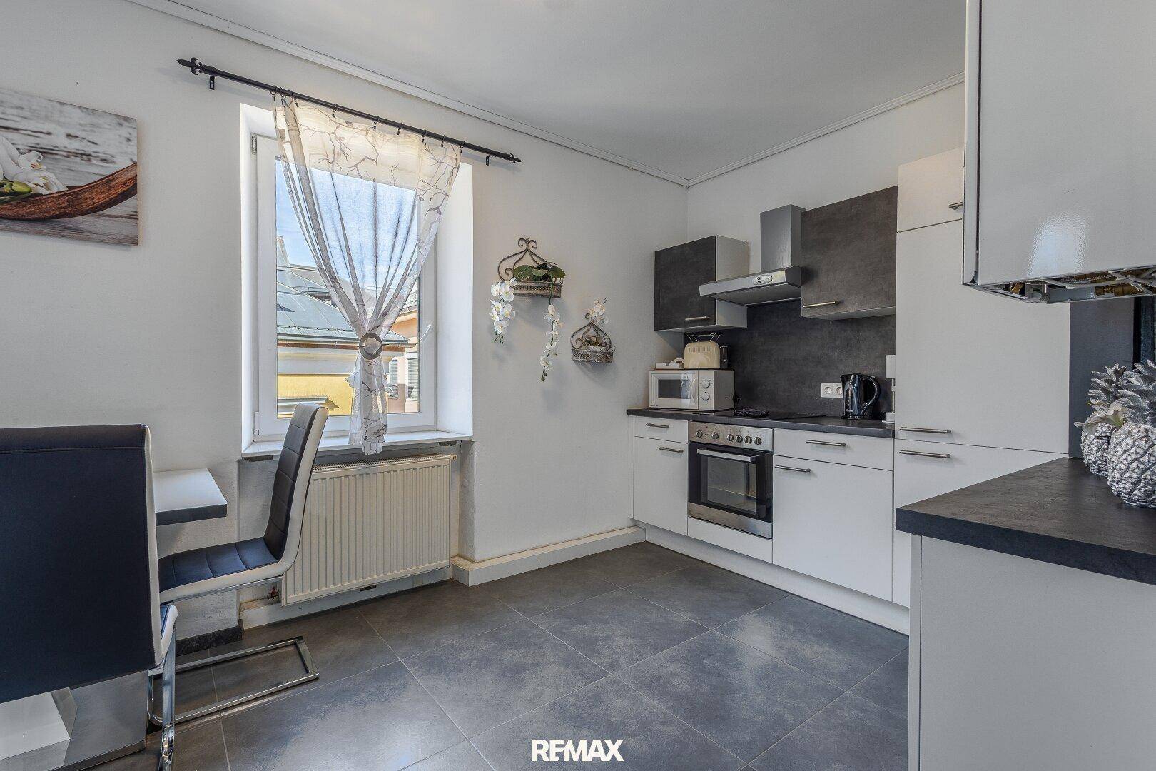 Helle Küche mit modernen weißen und grauen Schränken, Fenster und Essbereich.