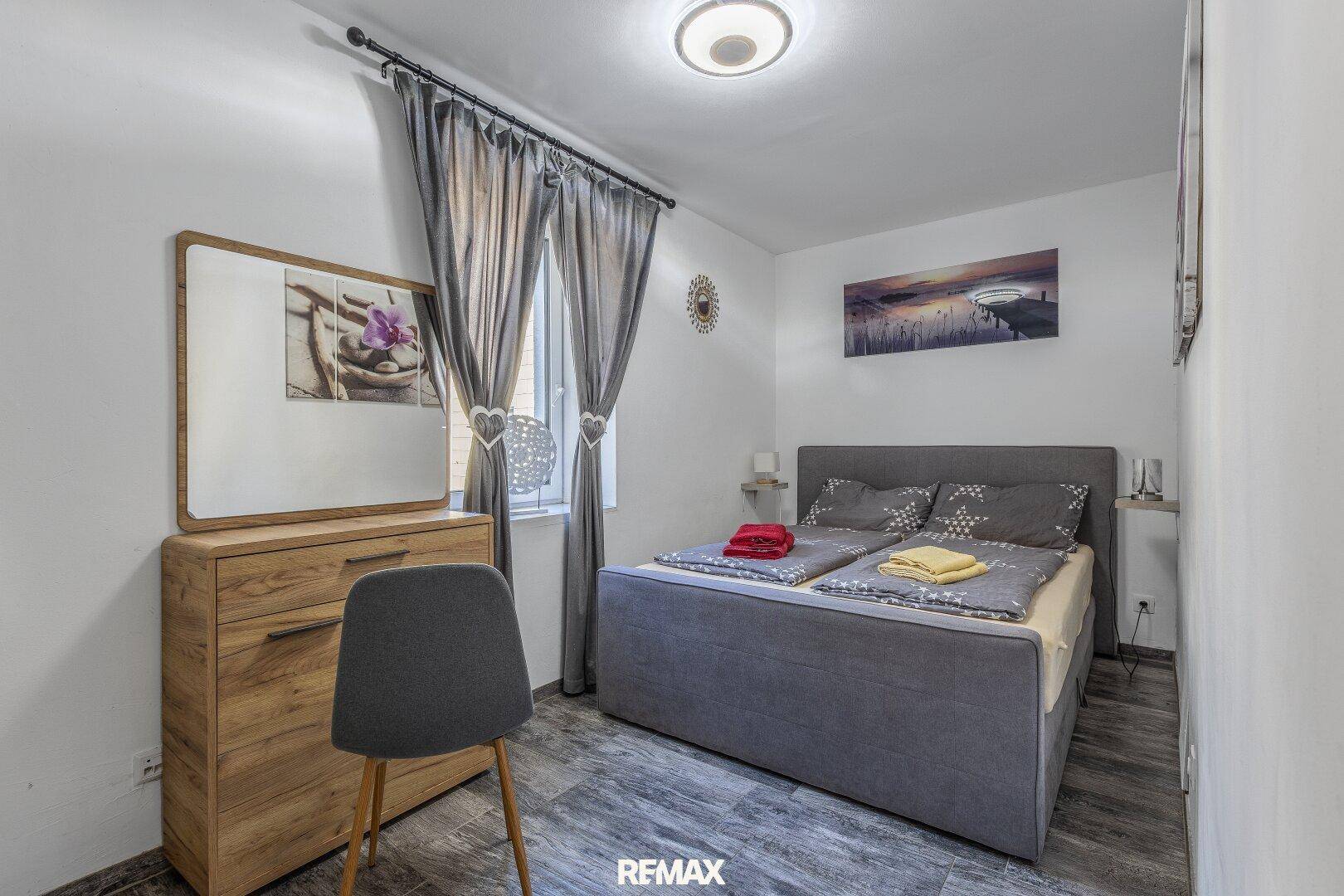 Gemütliches Schlafzimmer mit Doppelbett, Holzkommode und Blick nach draußen.