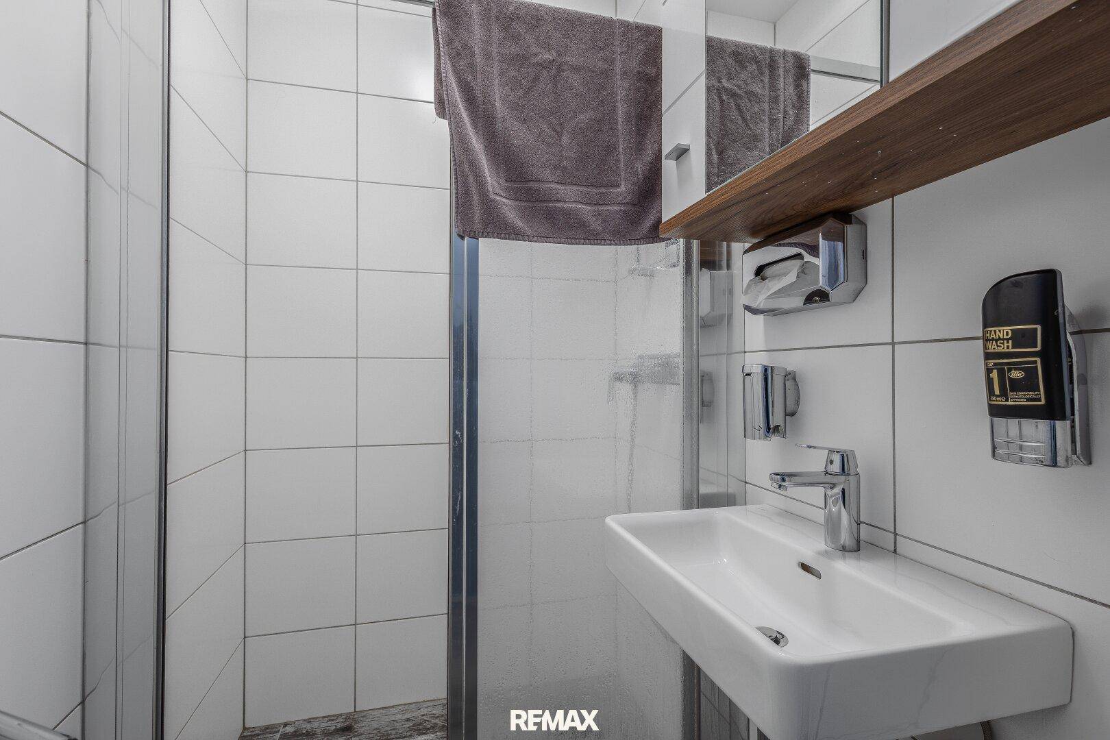 Kleines Badezimmer mit Waschbecken und Duschkabine, komplett gefliest in Weiß.