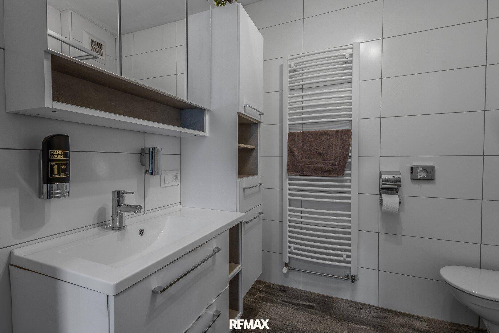 Modernes Badezimmer mit Waschtisch, Spiegelschrank, Handtuchheizkörper und weißen Fliesen.