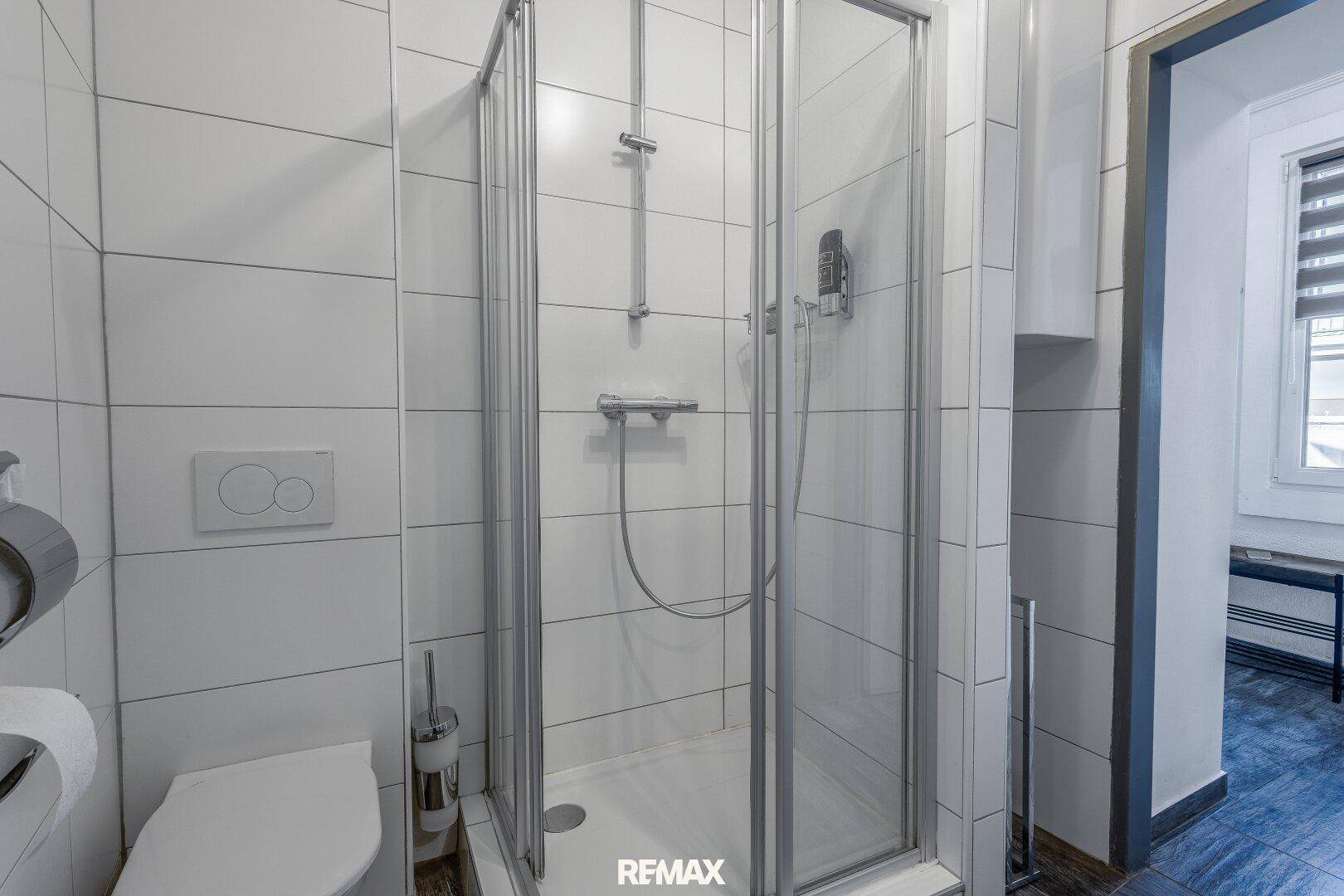Duschbereich im Badezimmer mit weißen Fliesen und einer modernen Glasduschkabine.