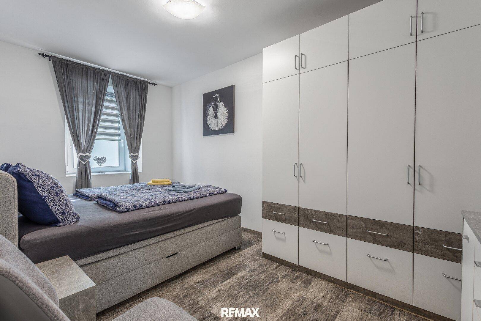 Helles Schlafzimmer mit Doppelbett, großem Kleiderschrank und Holzoptik-Laminatboden.