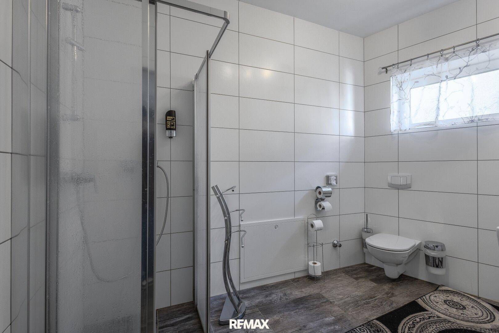 Geräumiges Badezimmer mit Duschkabine, WC und Fenster für natürliche Belüftung.