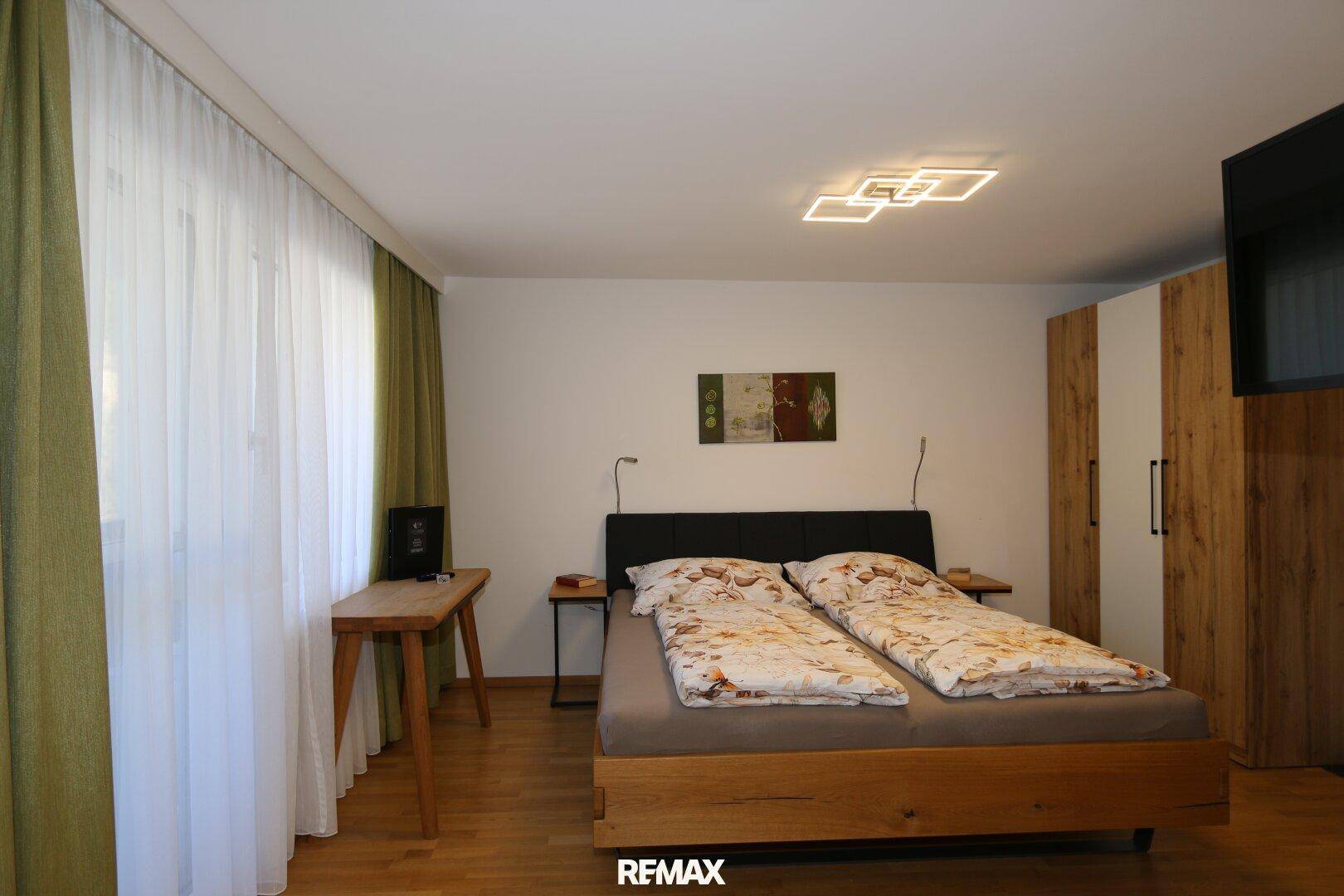 Helles Schlafzimmer mit Doppelbett, Holzboden und großen Fenstern für eine angenehme Atmosphäre.