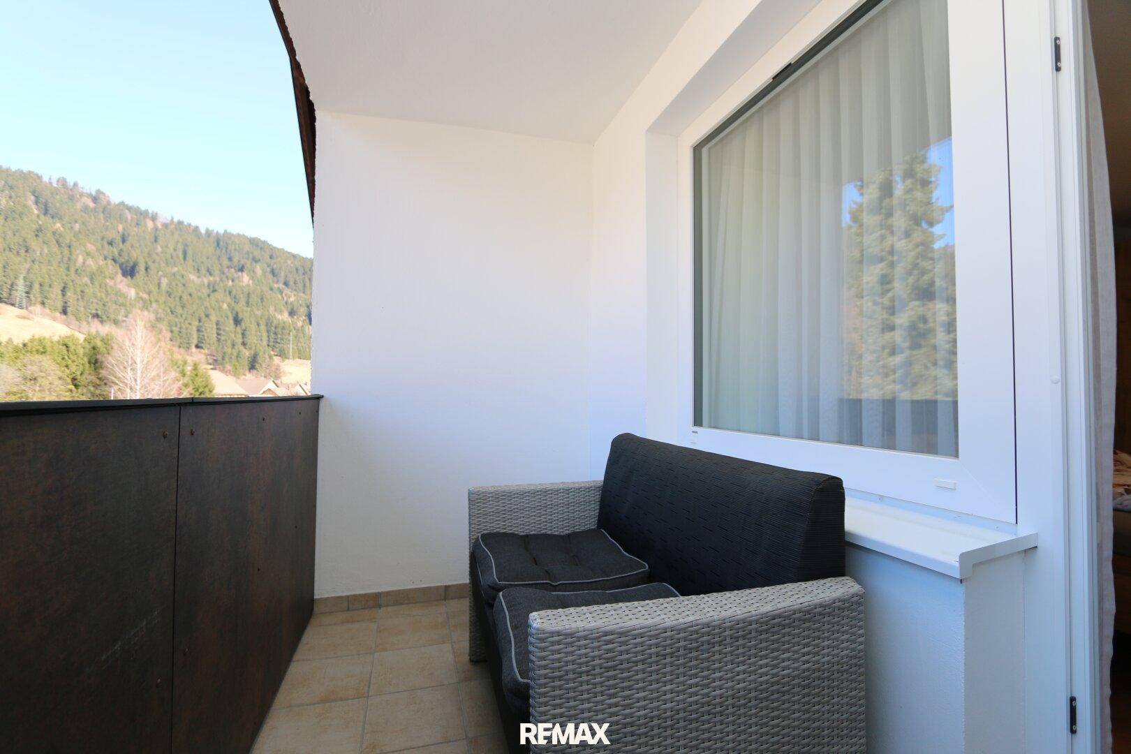Balkon mit bequemer Sitzbank und Blick auf die bewaldeten Hügel in der Ferne.