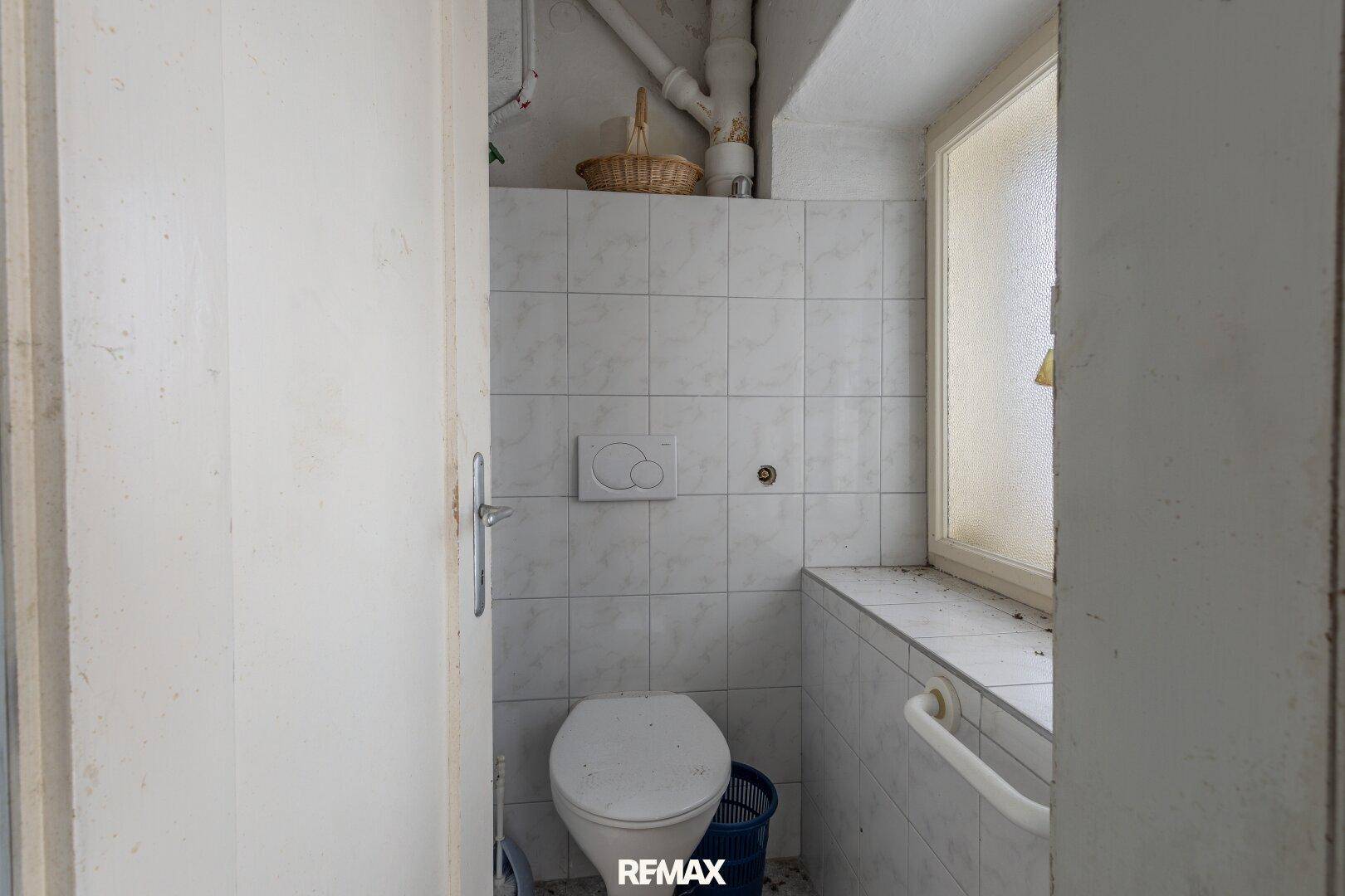 Kleines WC mit Toilette, gefliesten Wänden und einem Fenster für natürliche Belüftung.
