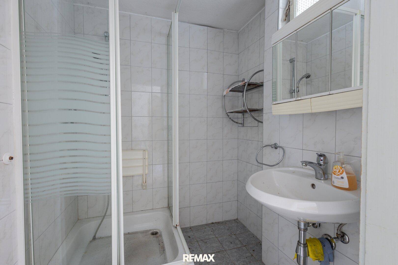 Badezimmer mit Duschkabine, Waschbecken und Spiegelschrank, in einfachem, funktionalem Zustand.