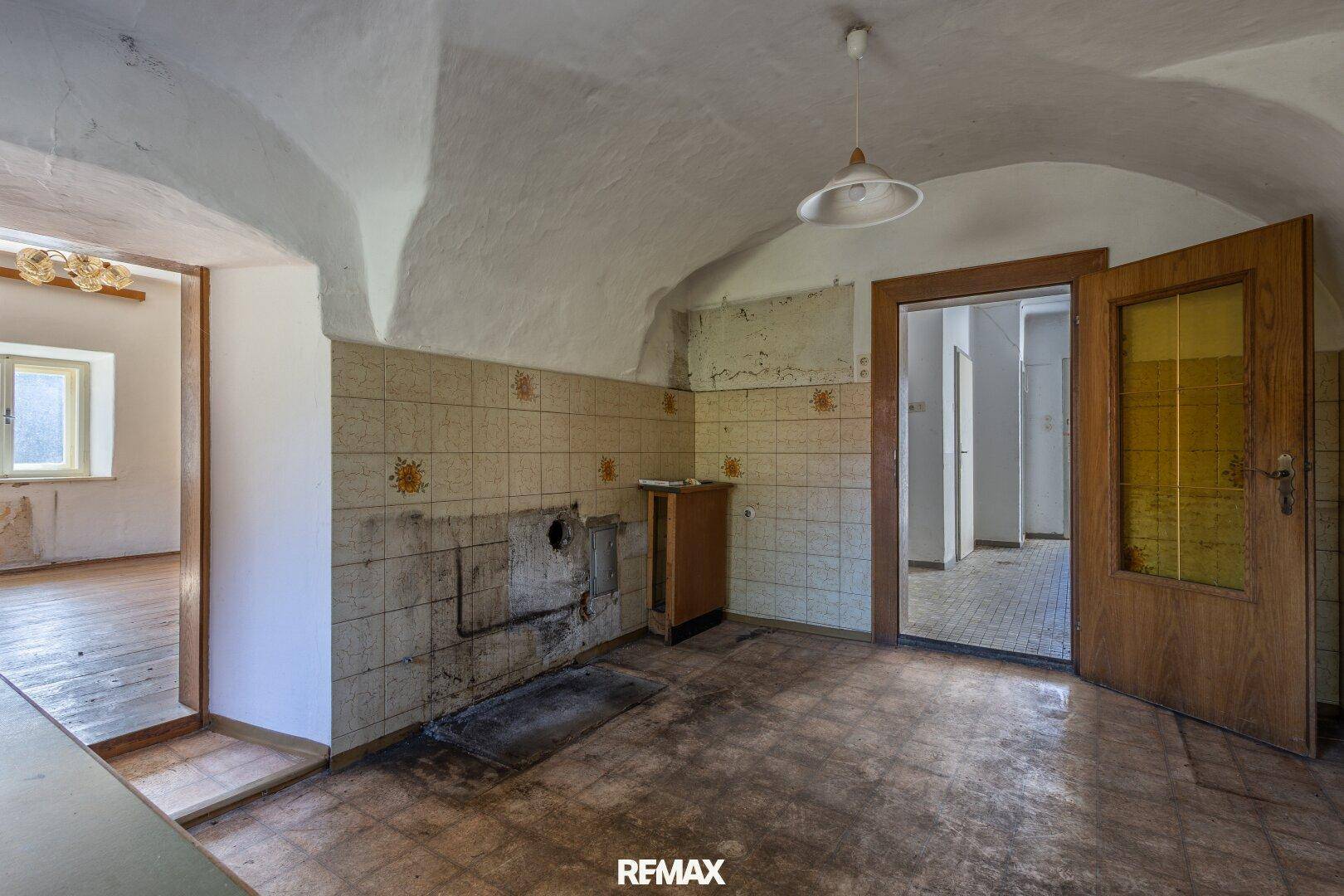 Küche mit Gewölbedecke, gefliesten Wänden und altem Herd, die eine umfassende Renovierung benötigt.