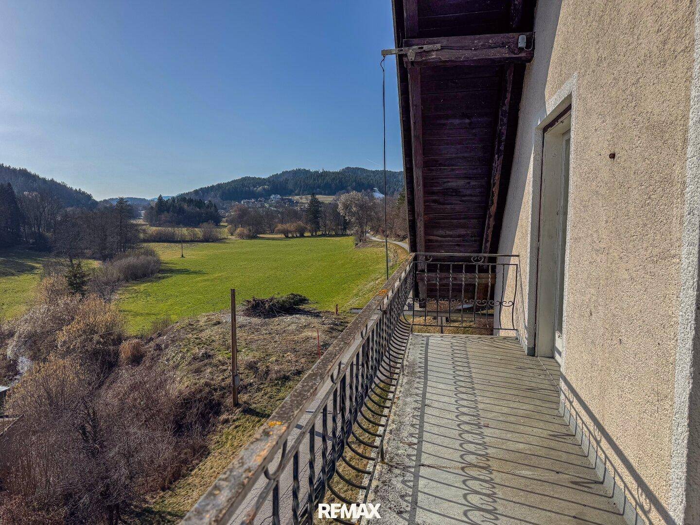 Langer Balkon mit schmiedeeisernem Geländer und weitem Blick über grüne Felder und Hügel.
