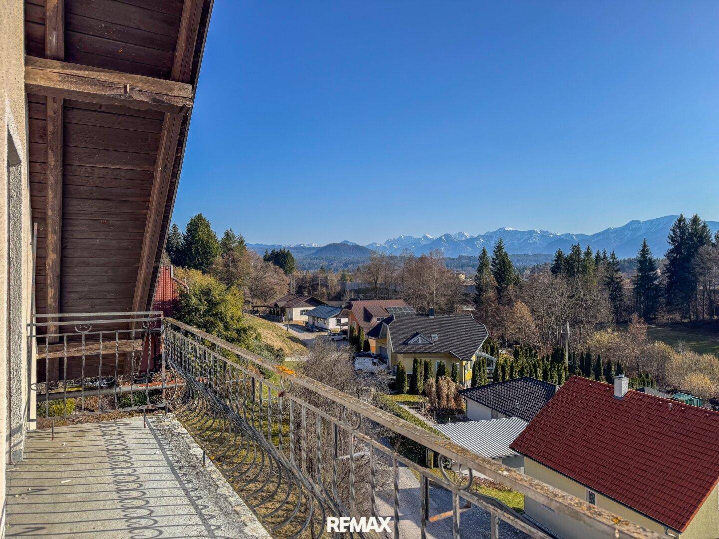 Blick vom Balkon mit schmiedeeisernem Geländer auf die umliegende Landschaft und Berge.