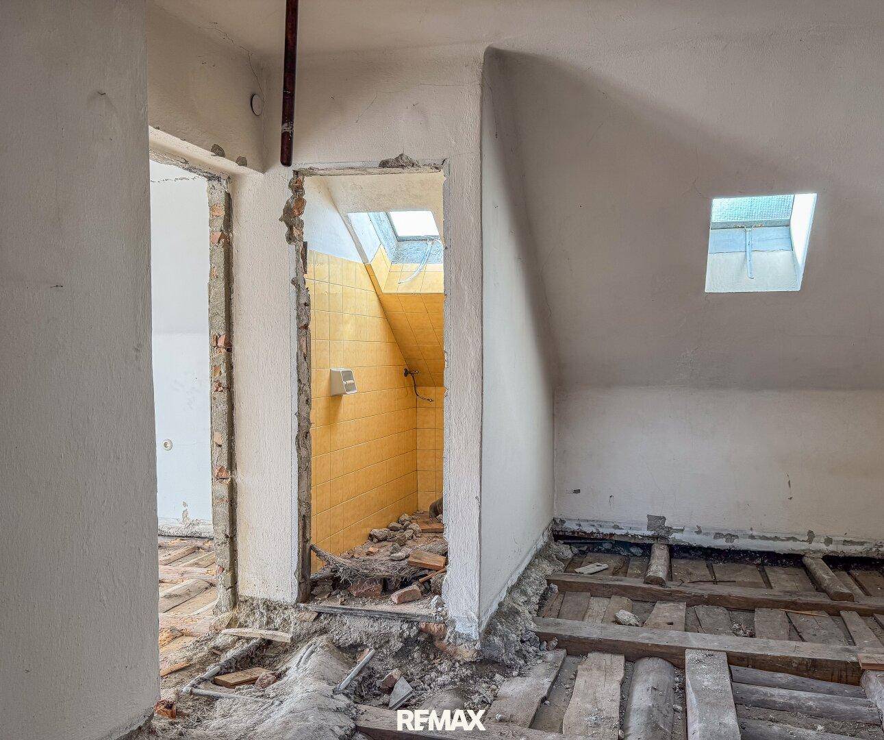 Innenraum im Rohbauzustand mit freiliegenden Holzbalken und Dachfenstern, bereit für die Renovierung.