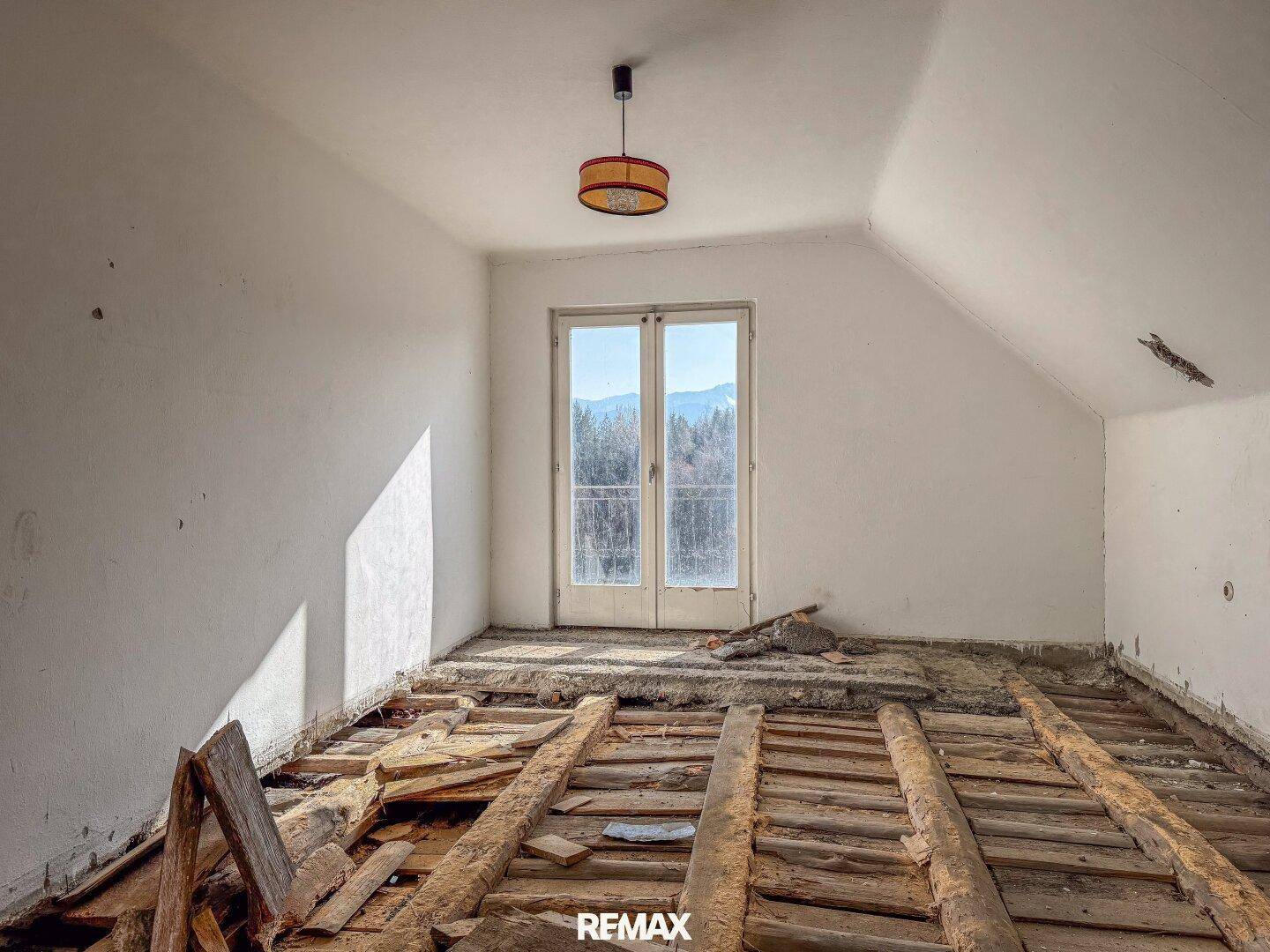 Dachzimmer im Rohbau mit freiliegenden Holzbalken und französischen Balkontüren mit Bergblick.