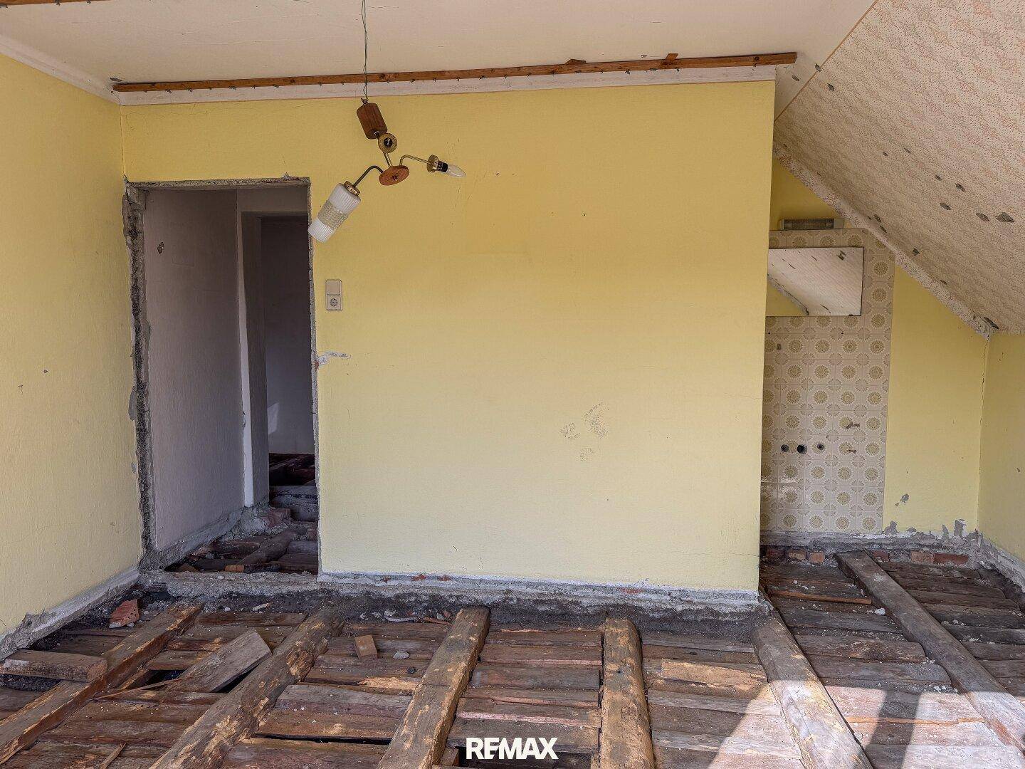 Gelber Innenraum im Rohbau mit freiliegenden Holzbalken und einer teilweise gefliesten Wand, bereit zur Neugestaltung.