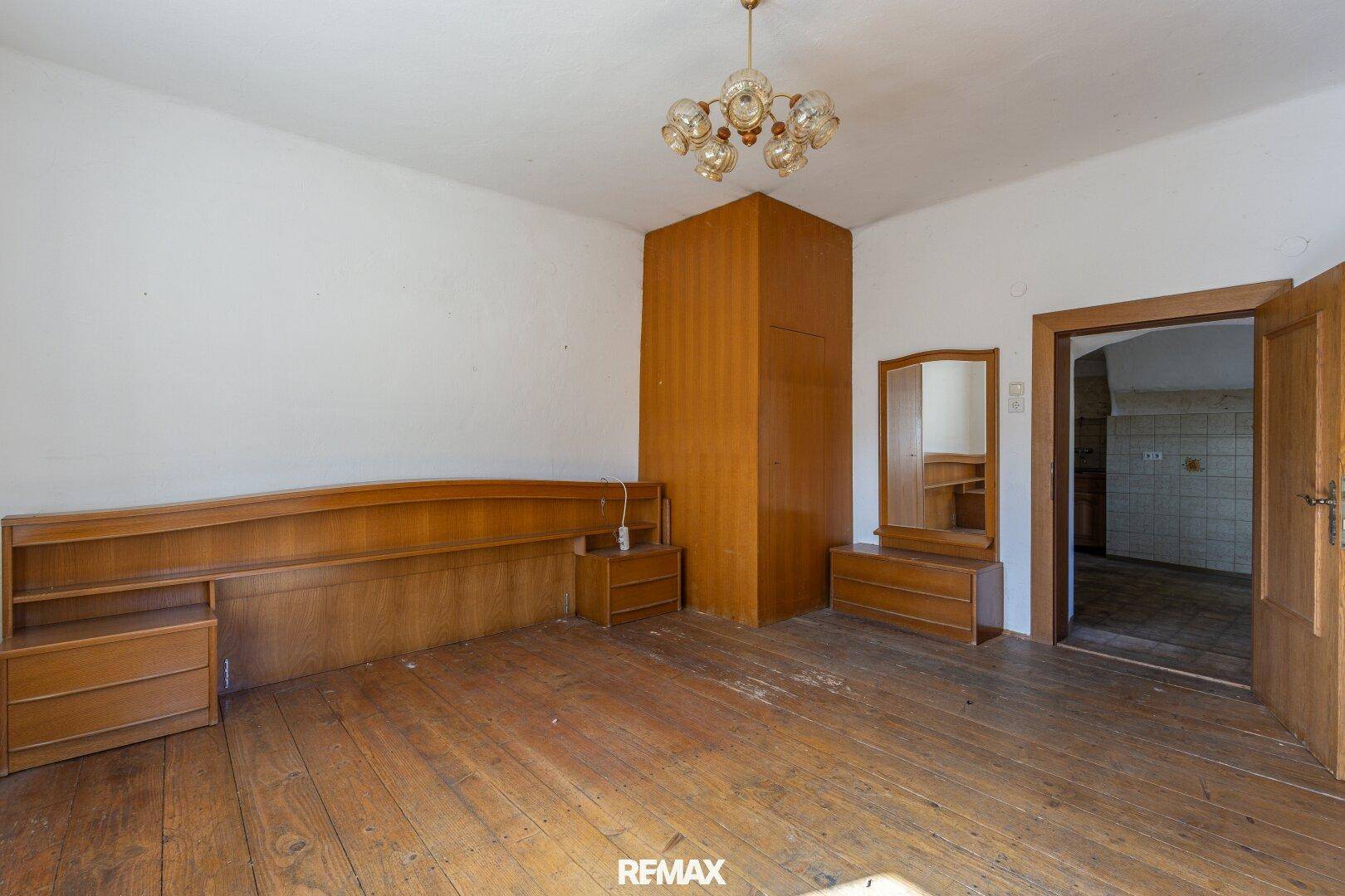 Geräumiges Schlafzimmer mit Holzdielen, Bettrahmen und Nachttischen, bereit für eine Renovierung.