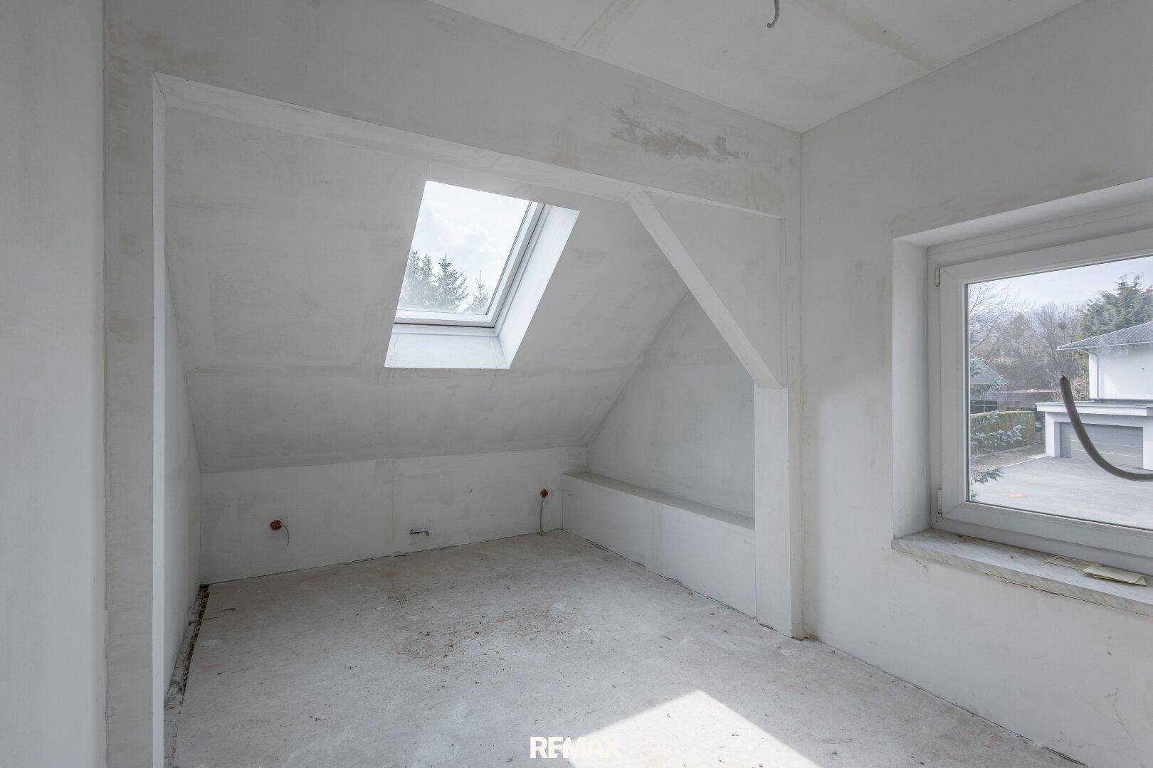 Unausgebauter Dachbodenraum mit Dachfenster und Rohbauwänden.