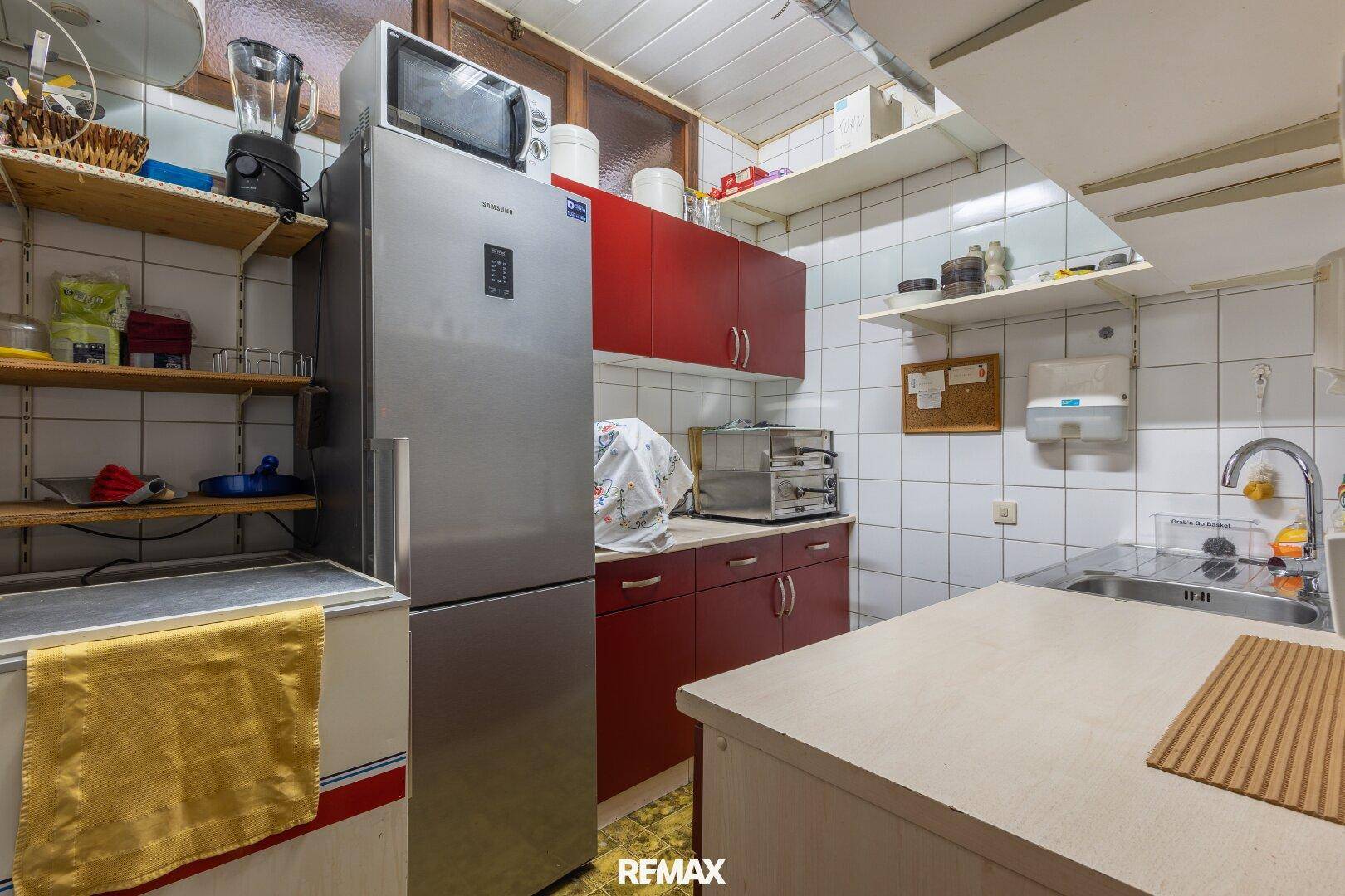 Einfache Küche mit roten Schränken, Kühlschrank und Fliesenwänden.