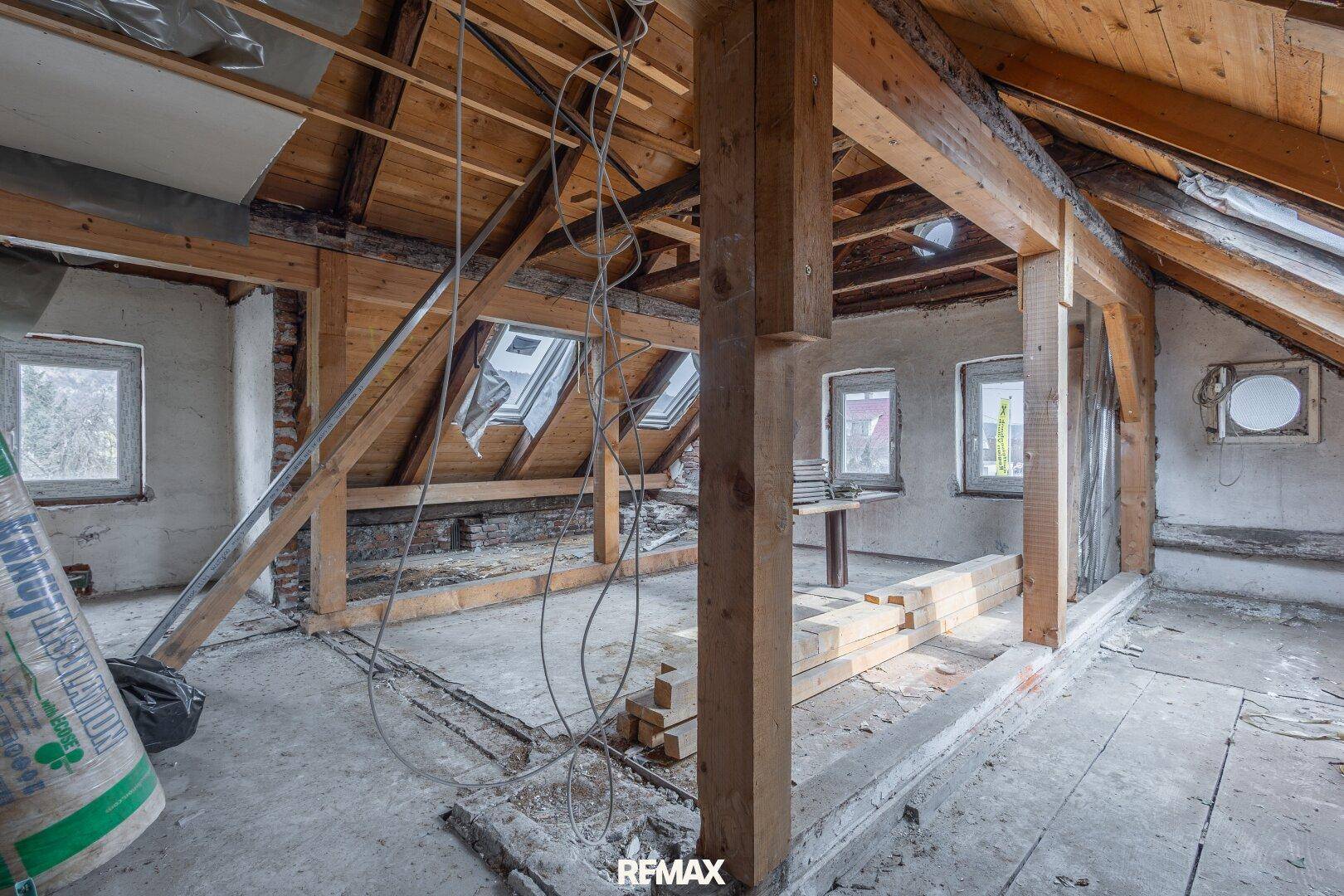 Offener Dachstuhl mit Holzbalken und Fenstern, bereit für den Ausbau.
