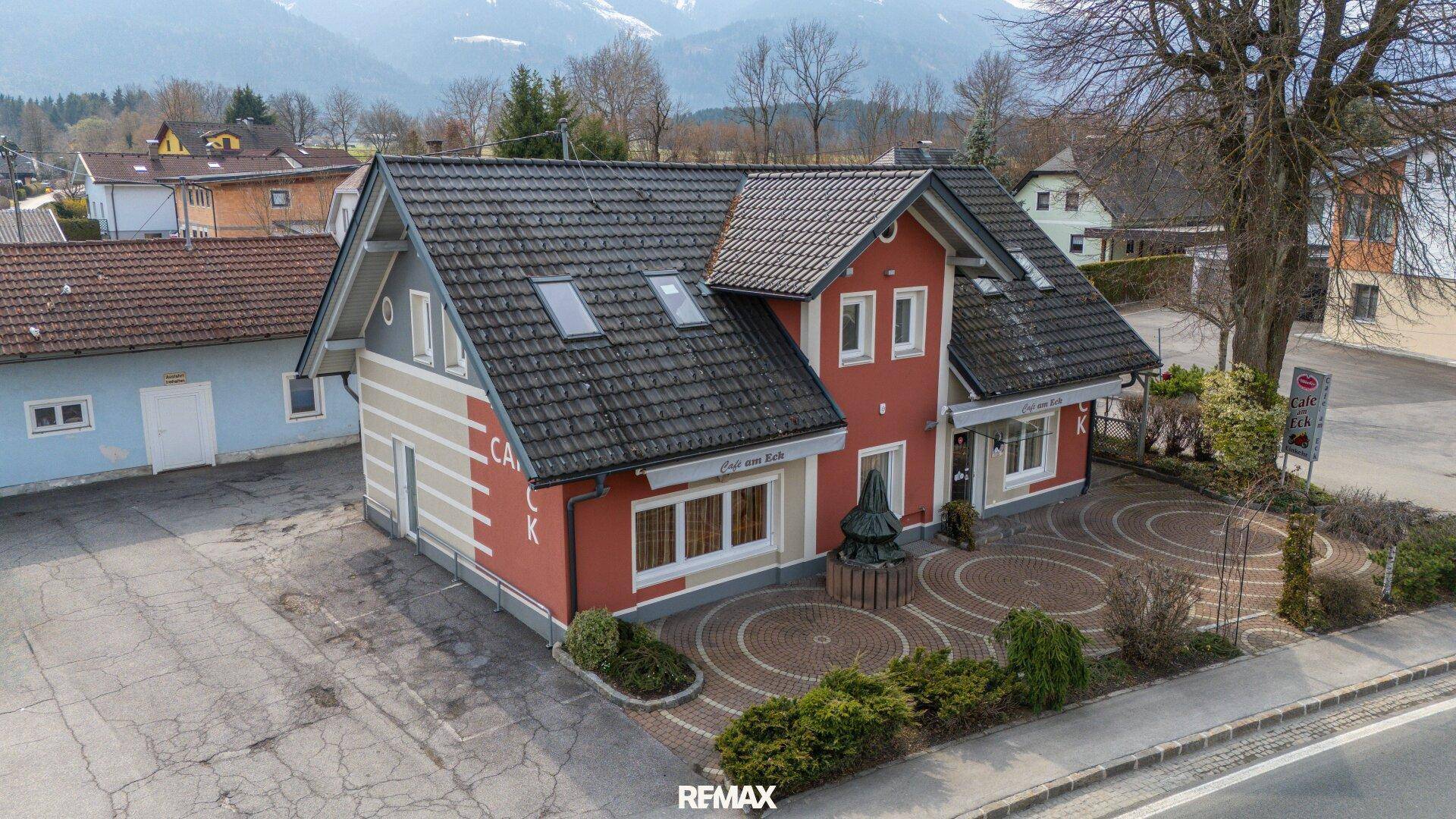 Luftaufnahme des gepflegten Gebäudes mit roter Fassade, Parkplätzen und Bergblick im Hintergrund.