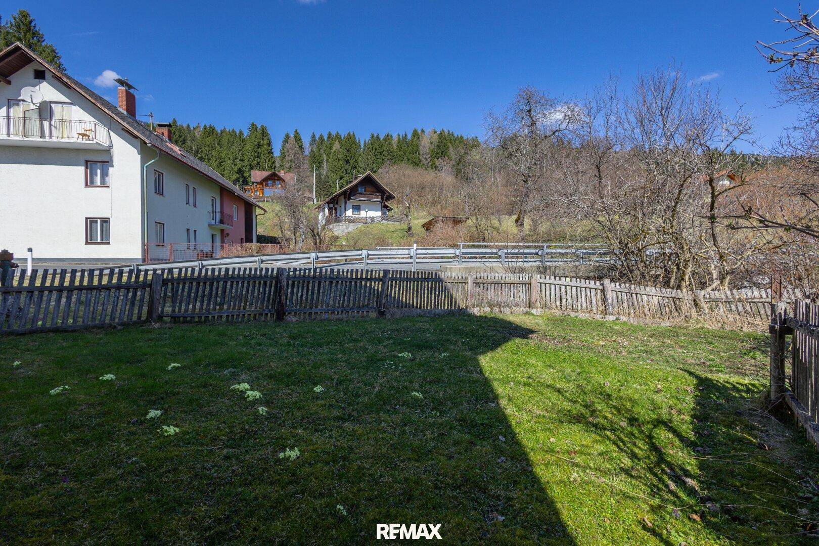 Großer Gartenbereich mit Holzzaun und Blick auf die umliegende grüne Landschaft.