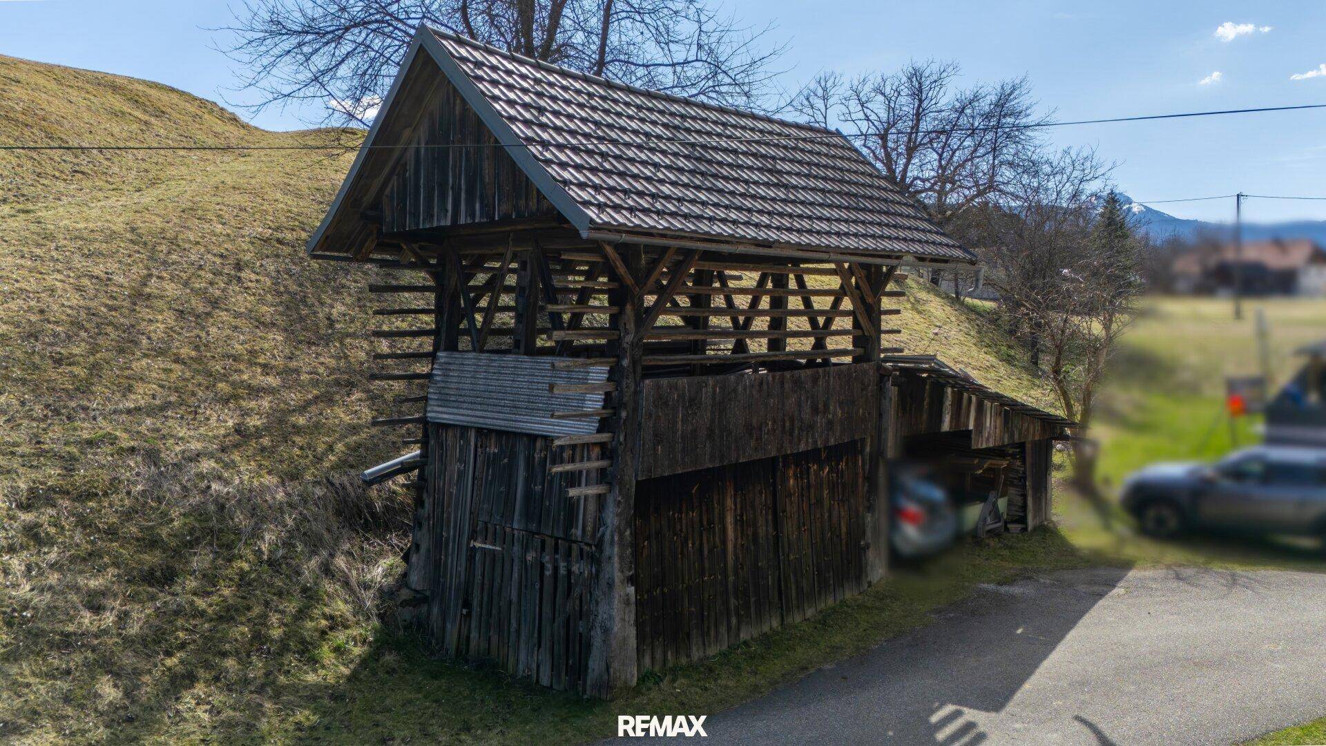 Rustikales Holzgebäude mit offenem Dachstuhl und angrenzendem Schuppen.