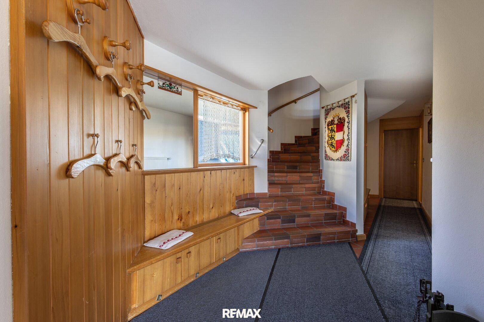 Gemütlicher Eingangsbereich mit Holzvertäfelung, Sitzbank und rustikaler Ziegeltreppe.