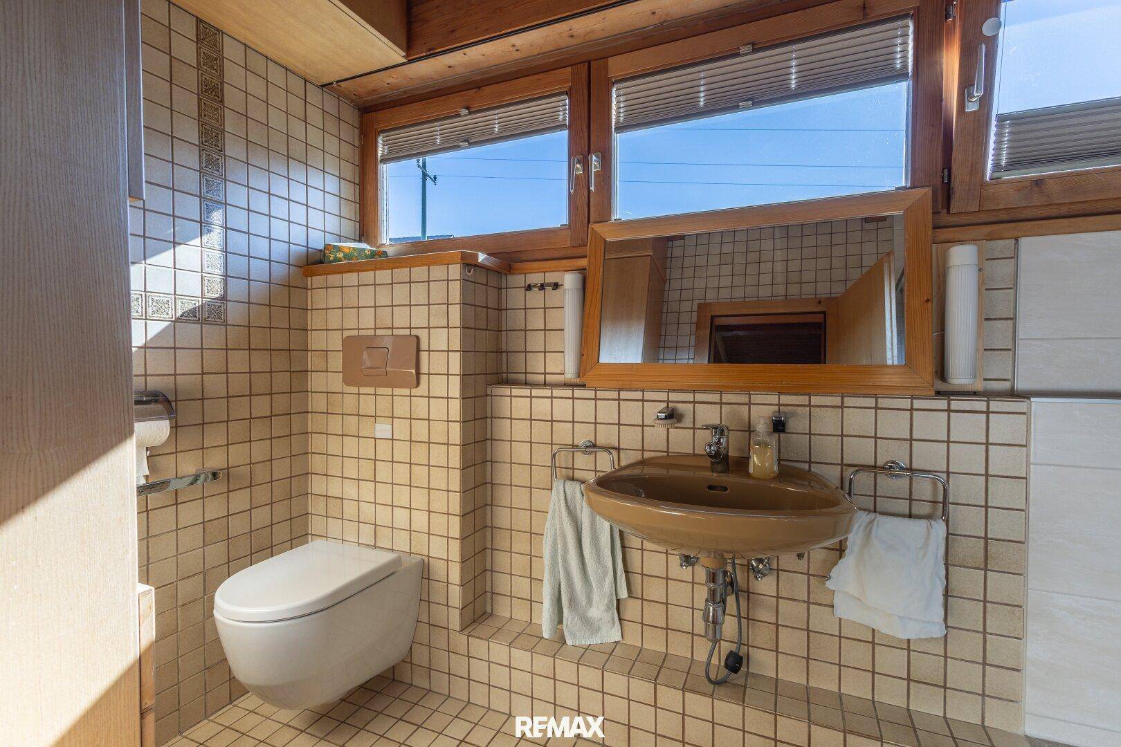 Badezimmer mit beigen Fliesen, Einzelwaschbecken und Wand-WC.