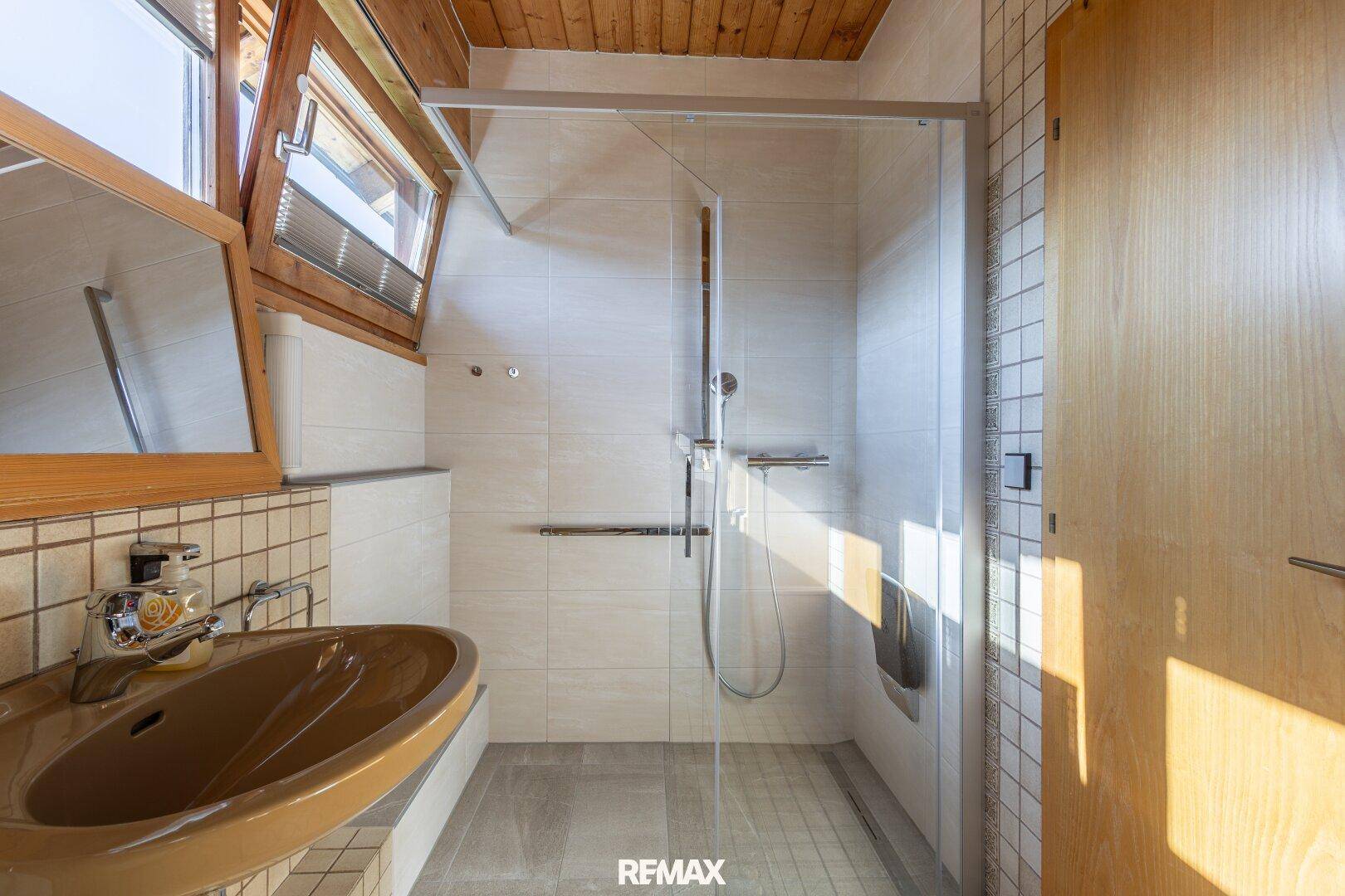 Badezimmer mit Duschkabine, braunem Waschbecken und Fenster für Tageslicht.