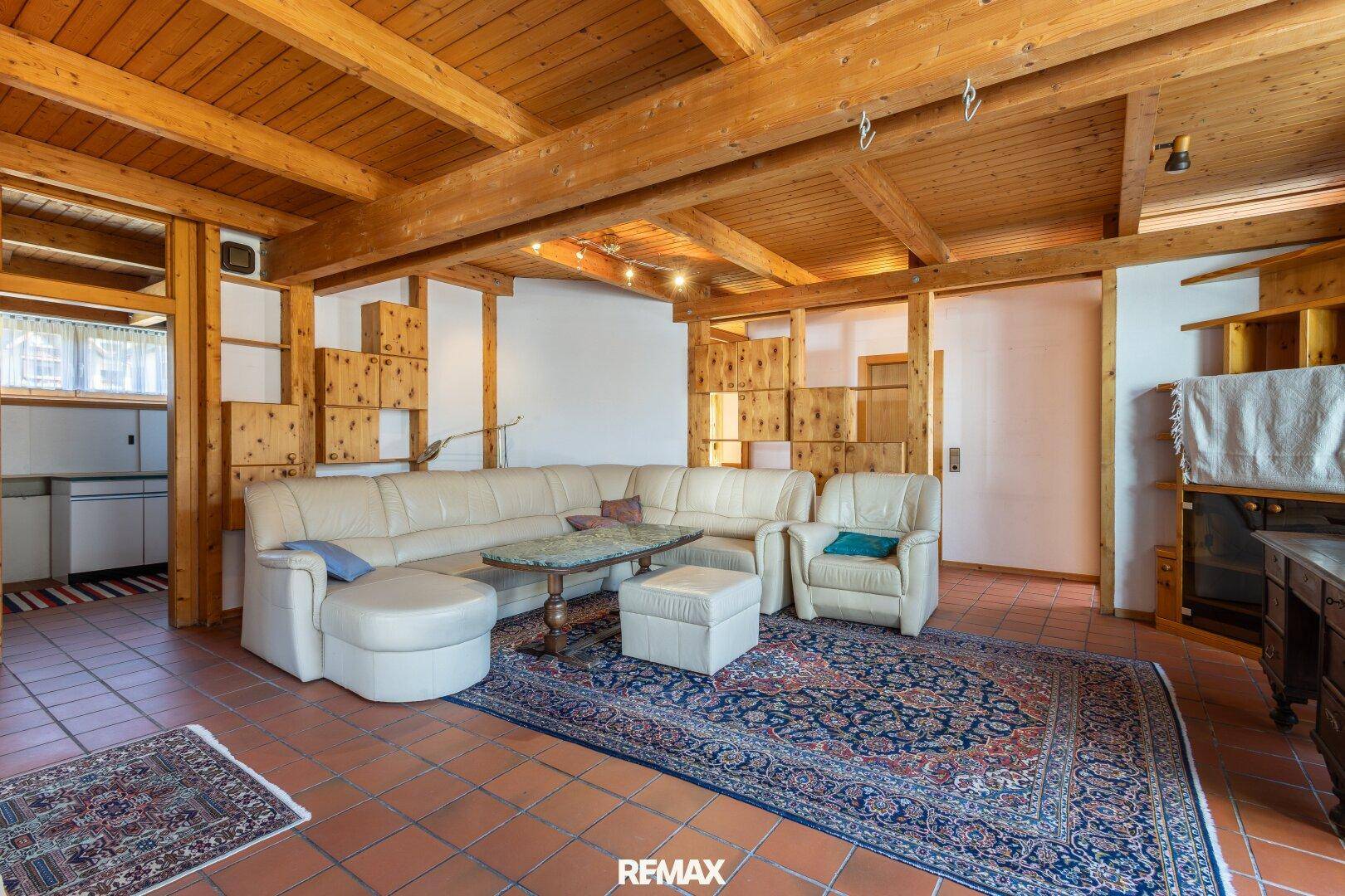 Helles Wohnzimmer mit Holzbalken, Terrakottafliesen und großem Teppich.
