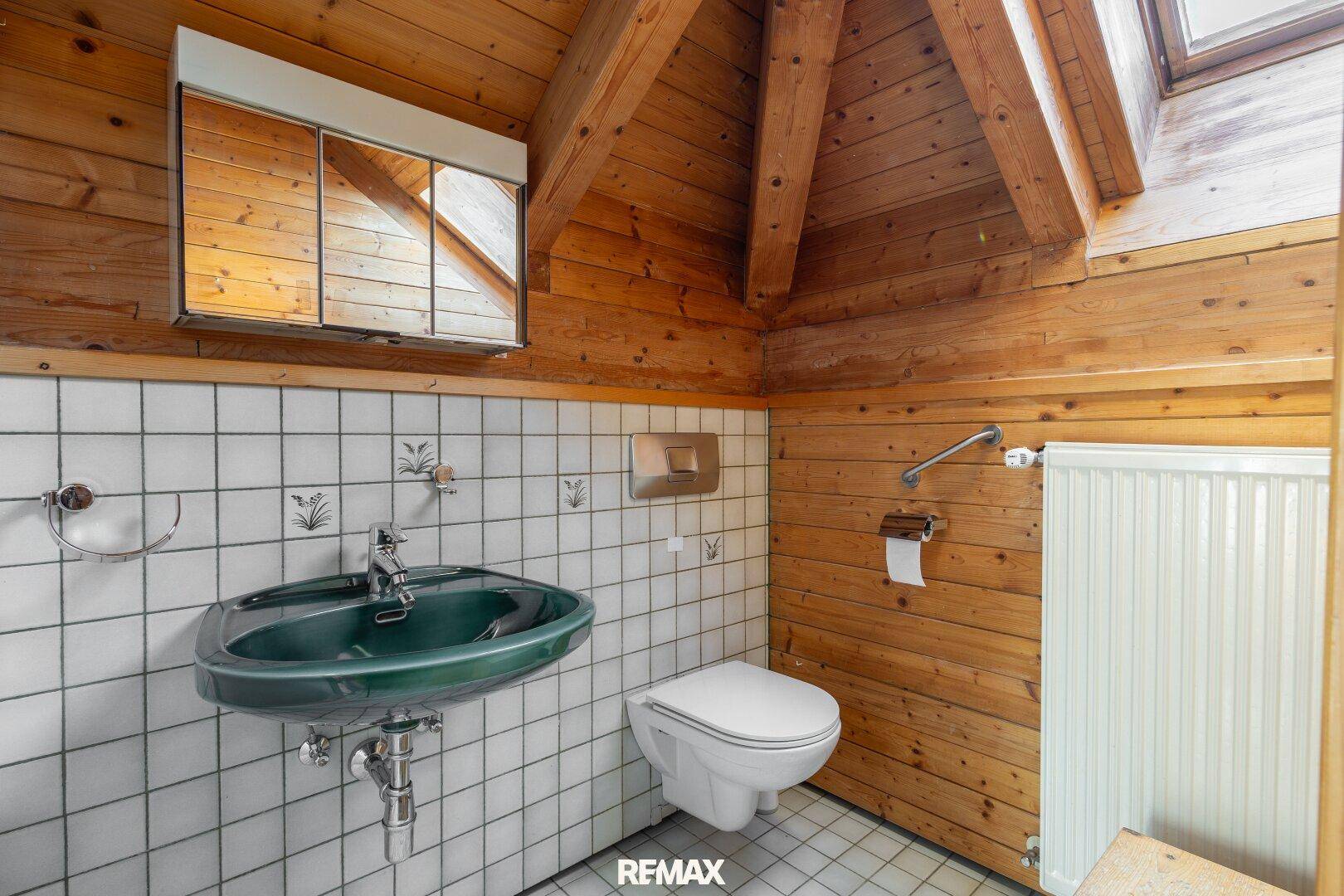 Badezimmer im Dachgeschoss mit Holzwänden, grüner Spüle und Dachfenster.