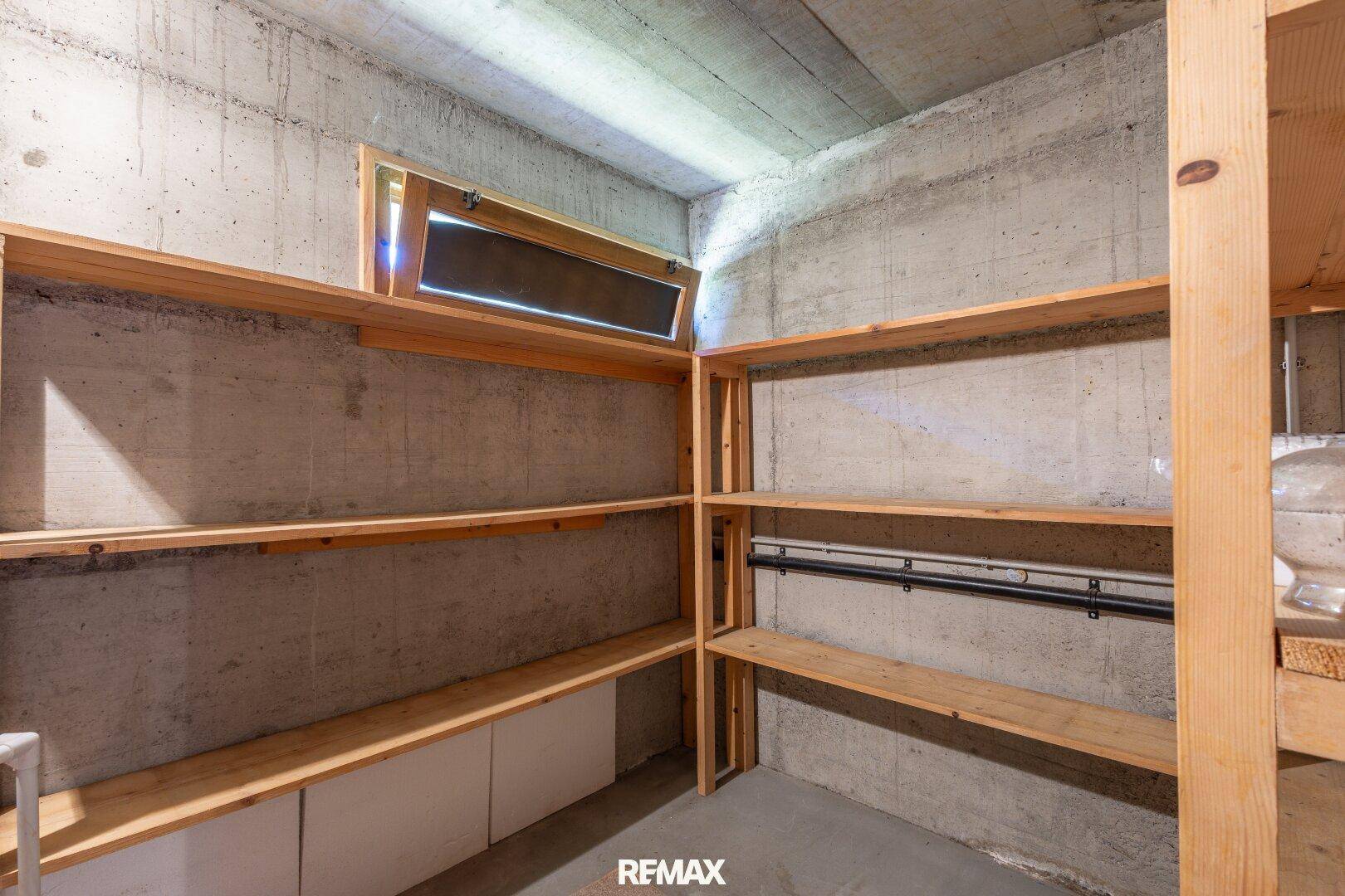 Kellerraum mit Betonwänden, Holzregalen und kleinem Fenster für Belüftung.
